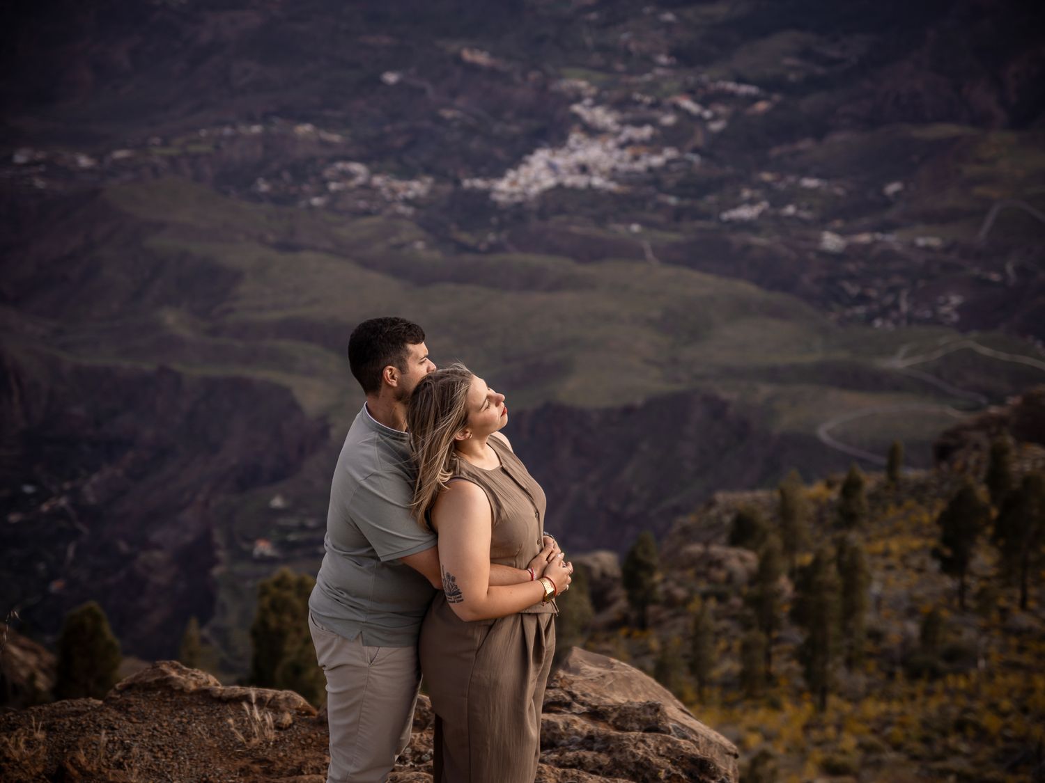 A couple shares an intimate moment overlooking a mountainous landscape at dusk.