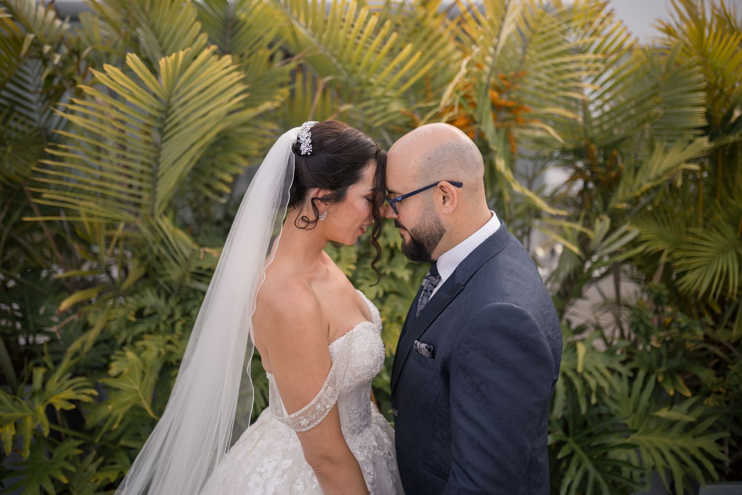 A romantic wedding portrait with the couple embracing among lush palm trees.