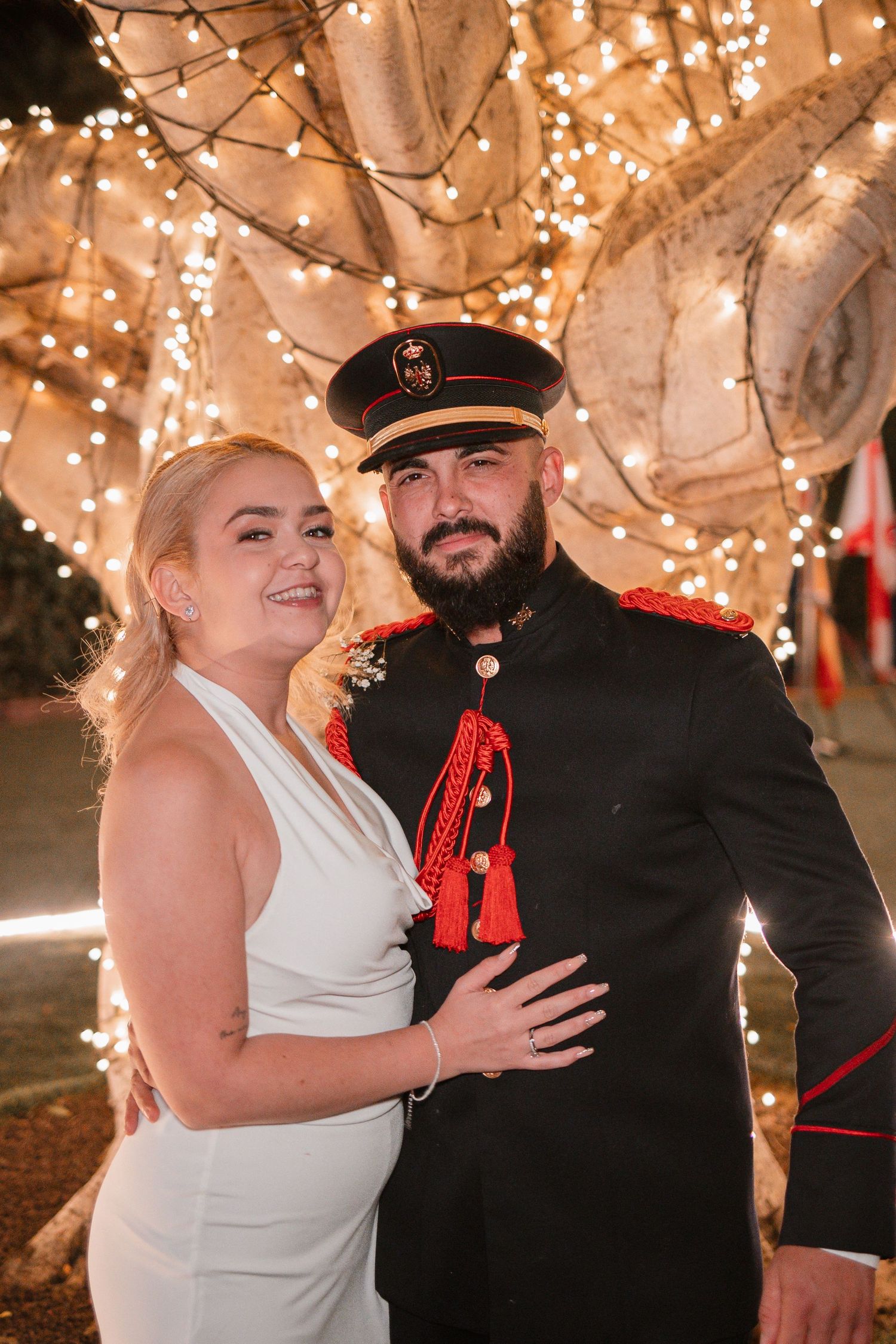 Wedding portrait under twinkling lights with decorated tree branches in the background.