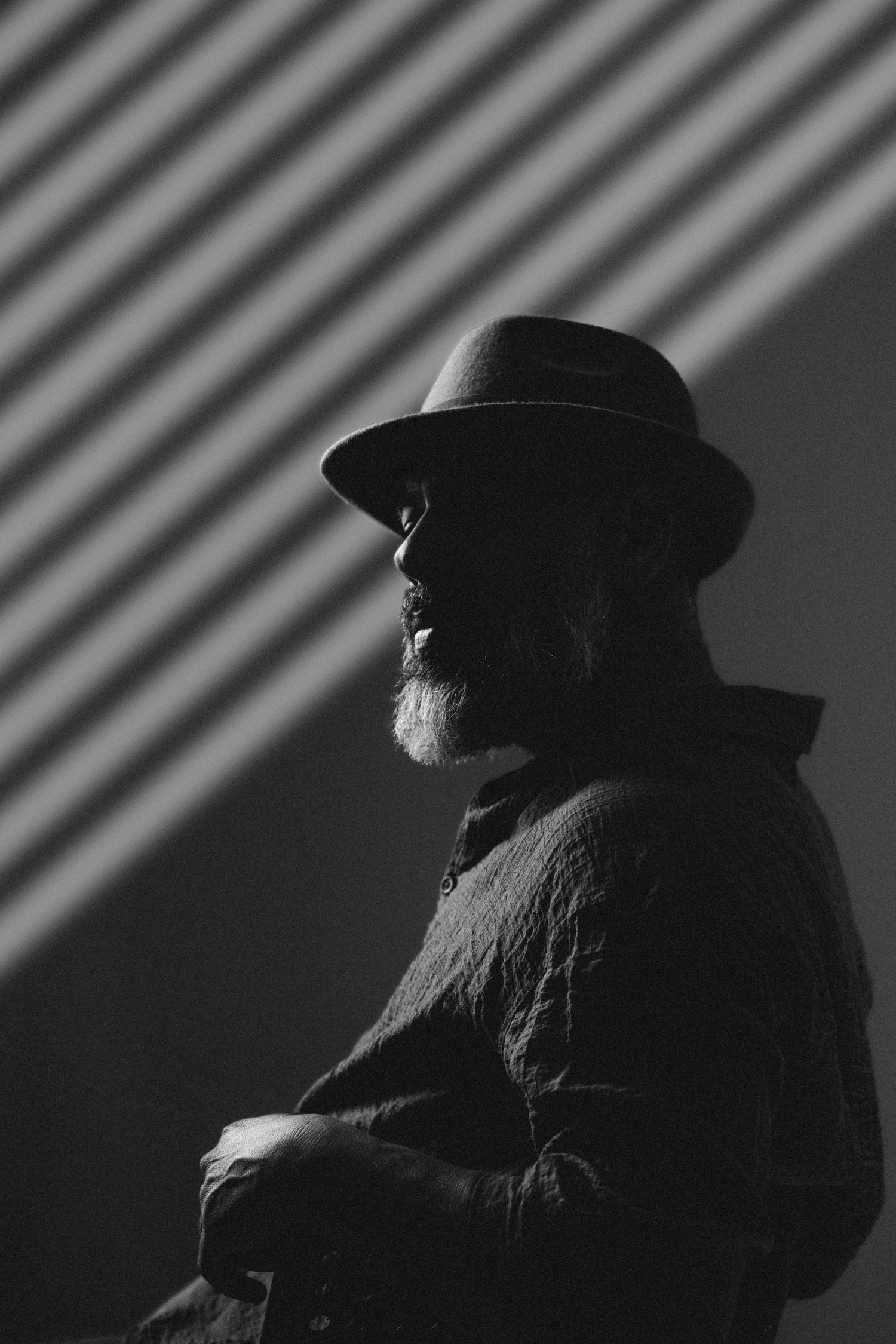 A dramatic black and white silhouette profile of a person wearing a hat, shown in a repeating pattern with shadows.