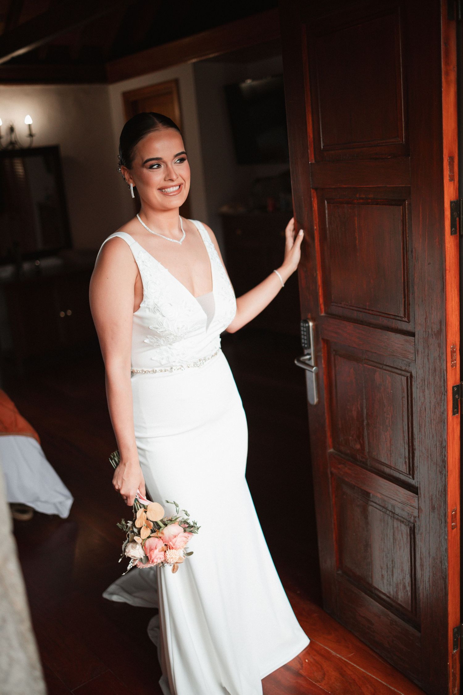 A bride in a classic white dress poses confidently against dark wooden doors.