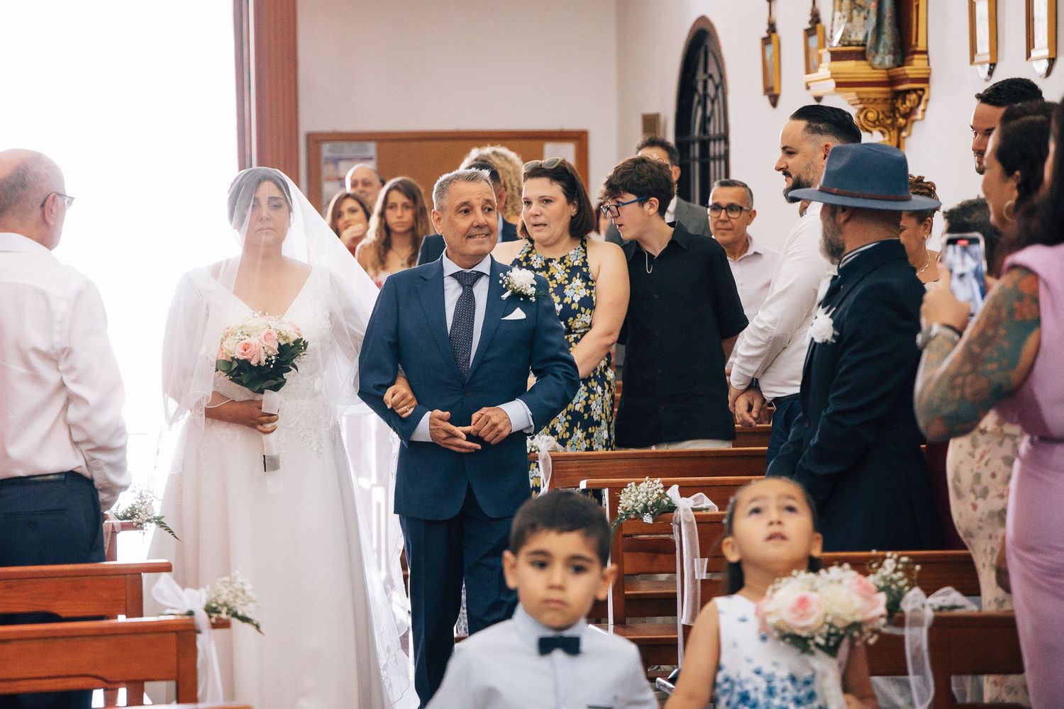 Bride and groom walking down church aisle during wedding ceremony with guests and flower girl.