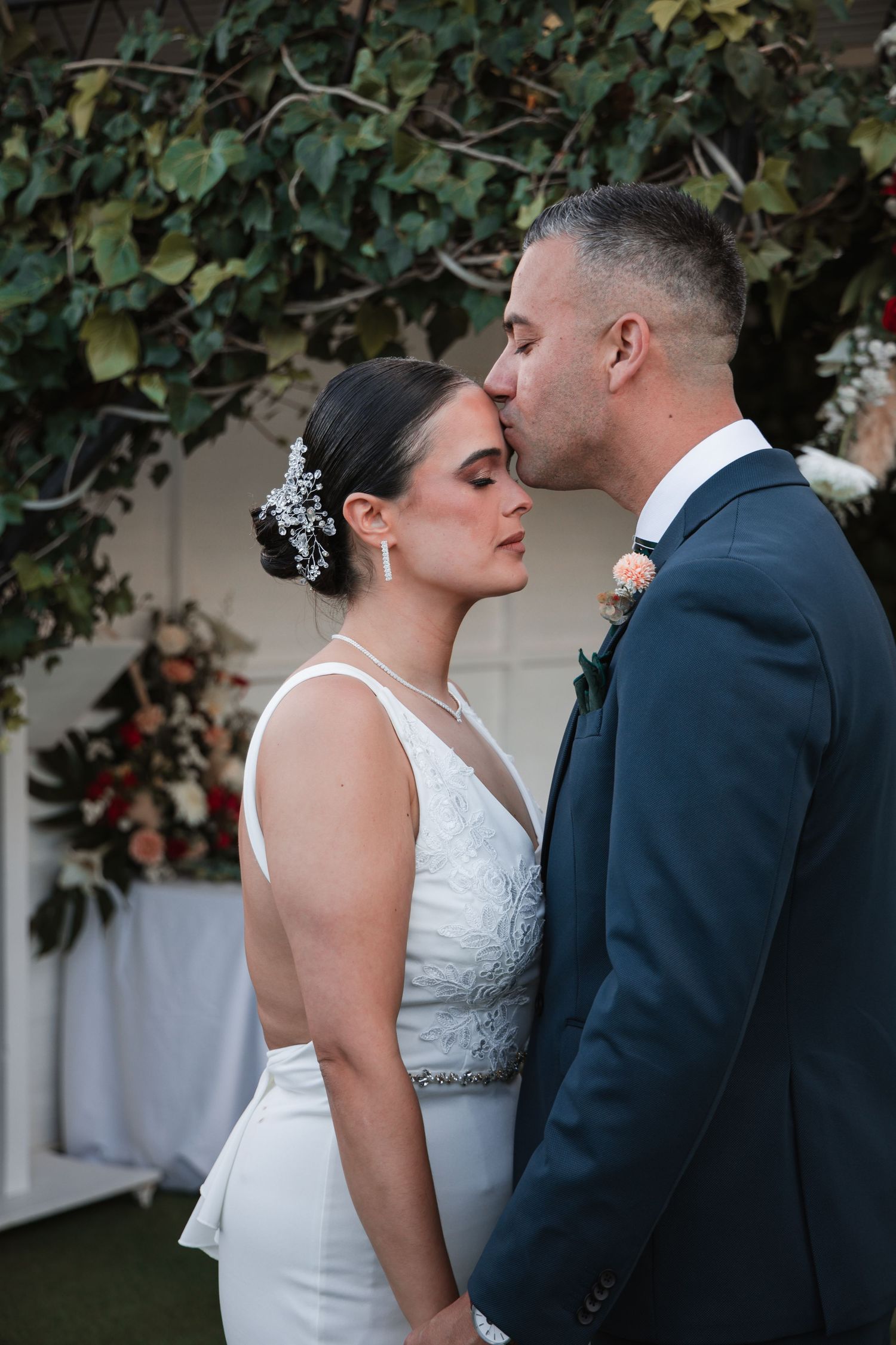 A romantic wedding couple shares intimate moments in a garden setting with ivy-covered walls.