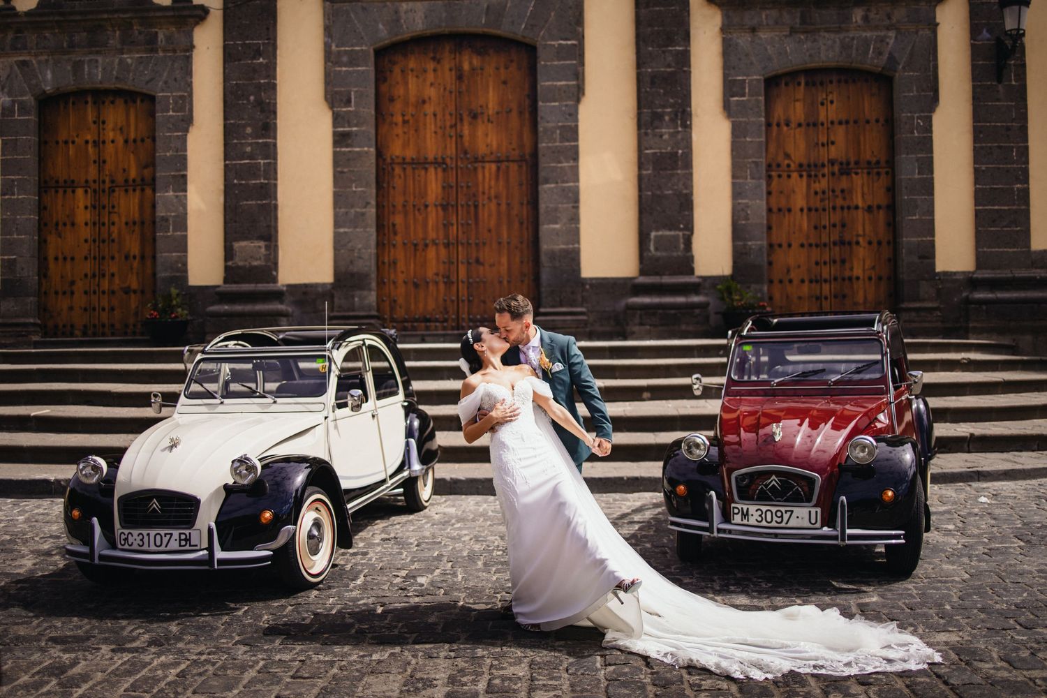 Classic vintage cars parked in front of stone archways create a romantic wedding scene.