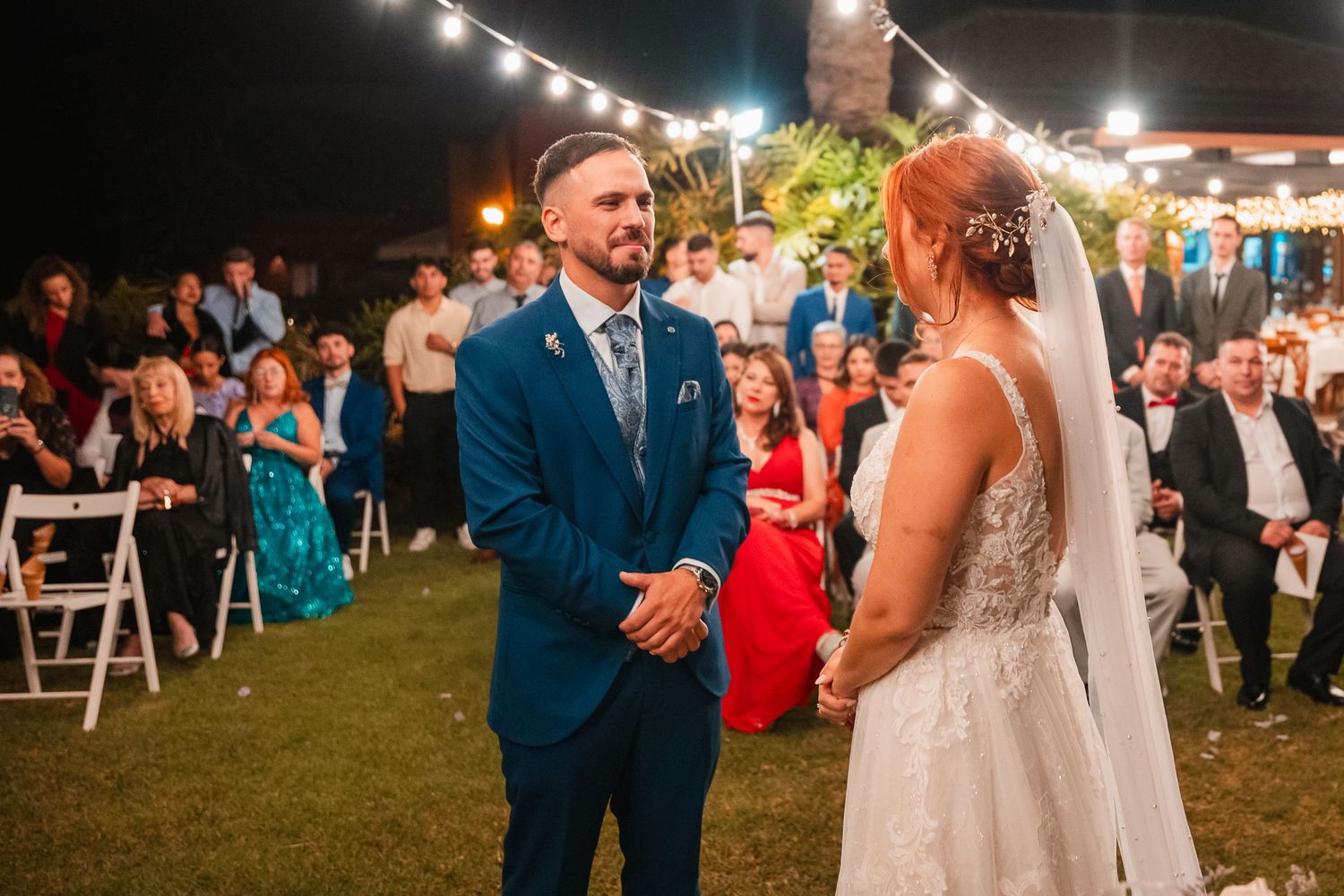 Wedding celebration under string lights with guests watching emotional moments.