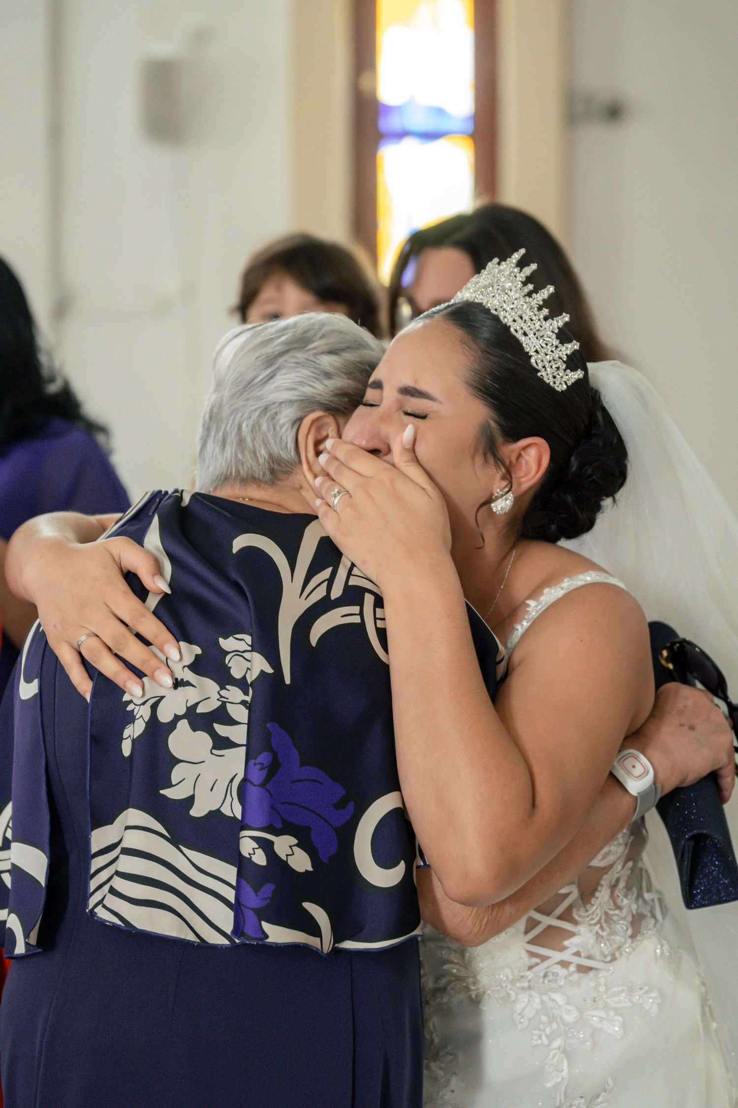 Emotional embrace between bride in white gown and family member wearing navy floral dress.
