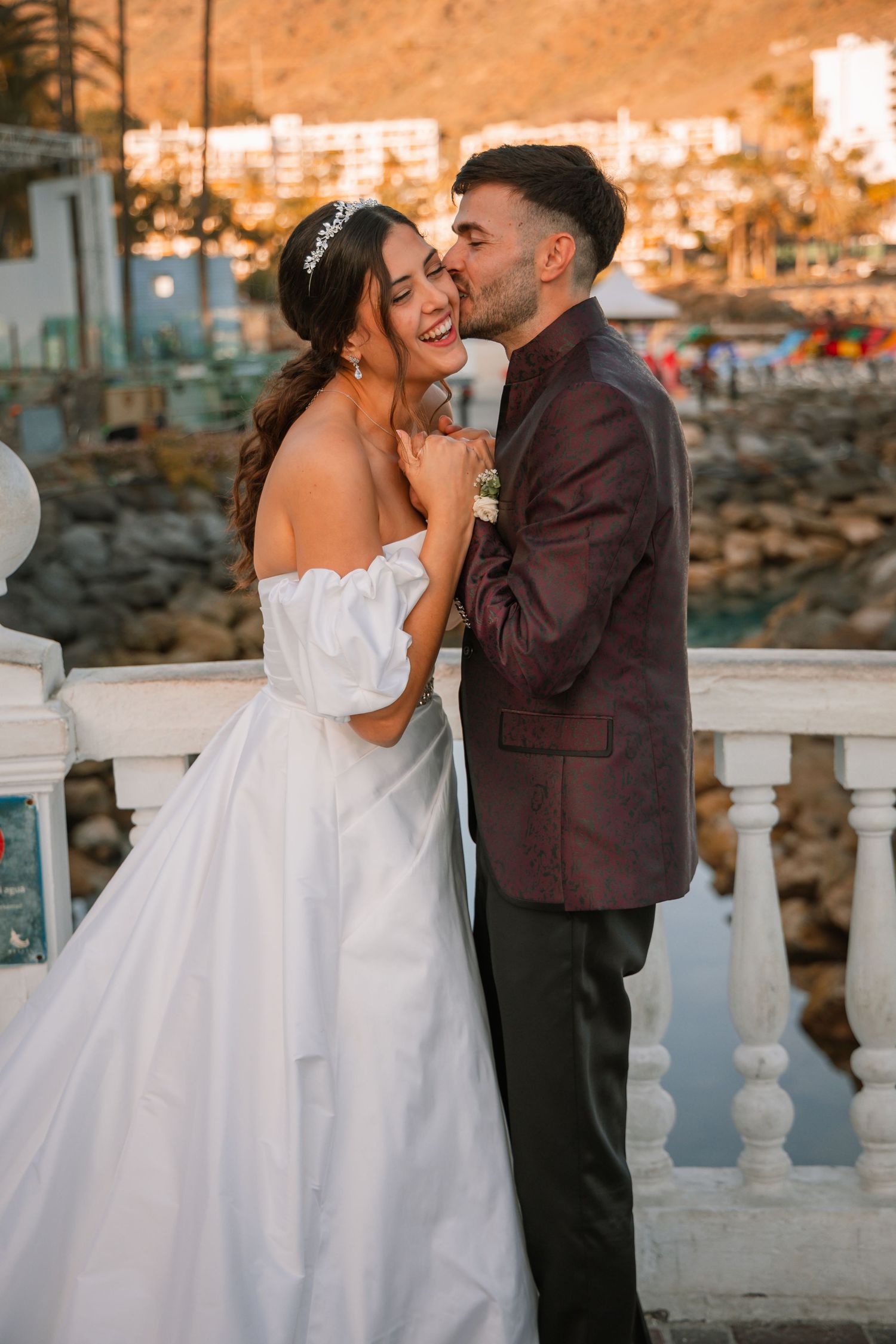 A joyful wedding moment captured on a balcony with a coastal town view at sunset.