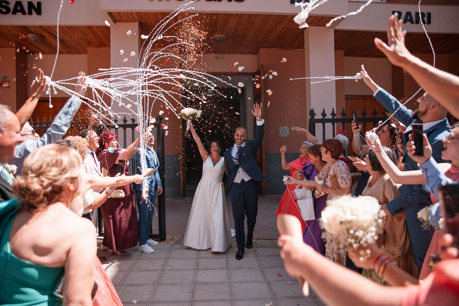 Wedding celebration with guests throwing confetti in an outdoor venue.