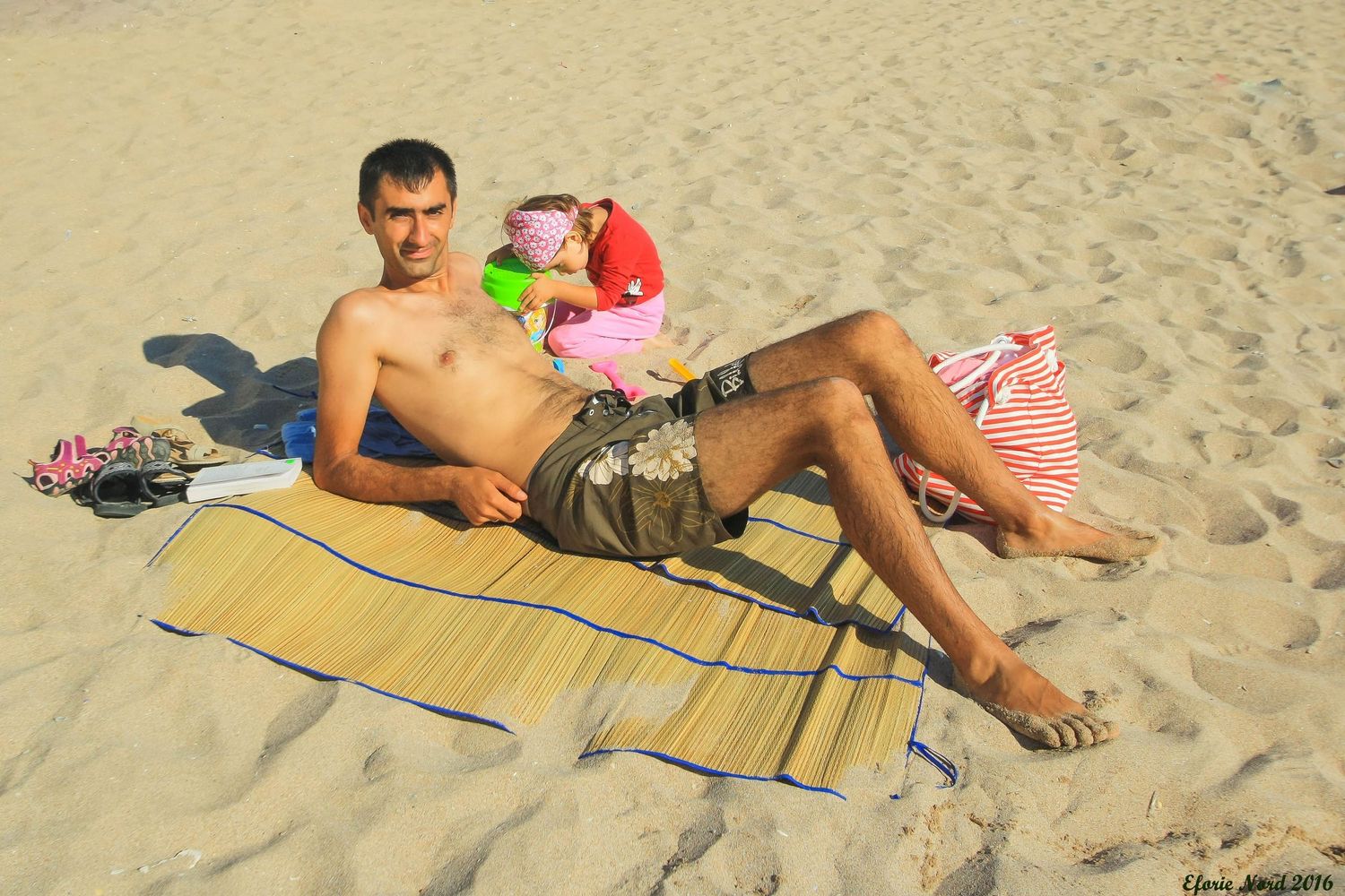 People relaxing on beach mats along a sandy shoreline on a sunny day.