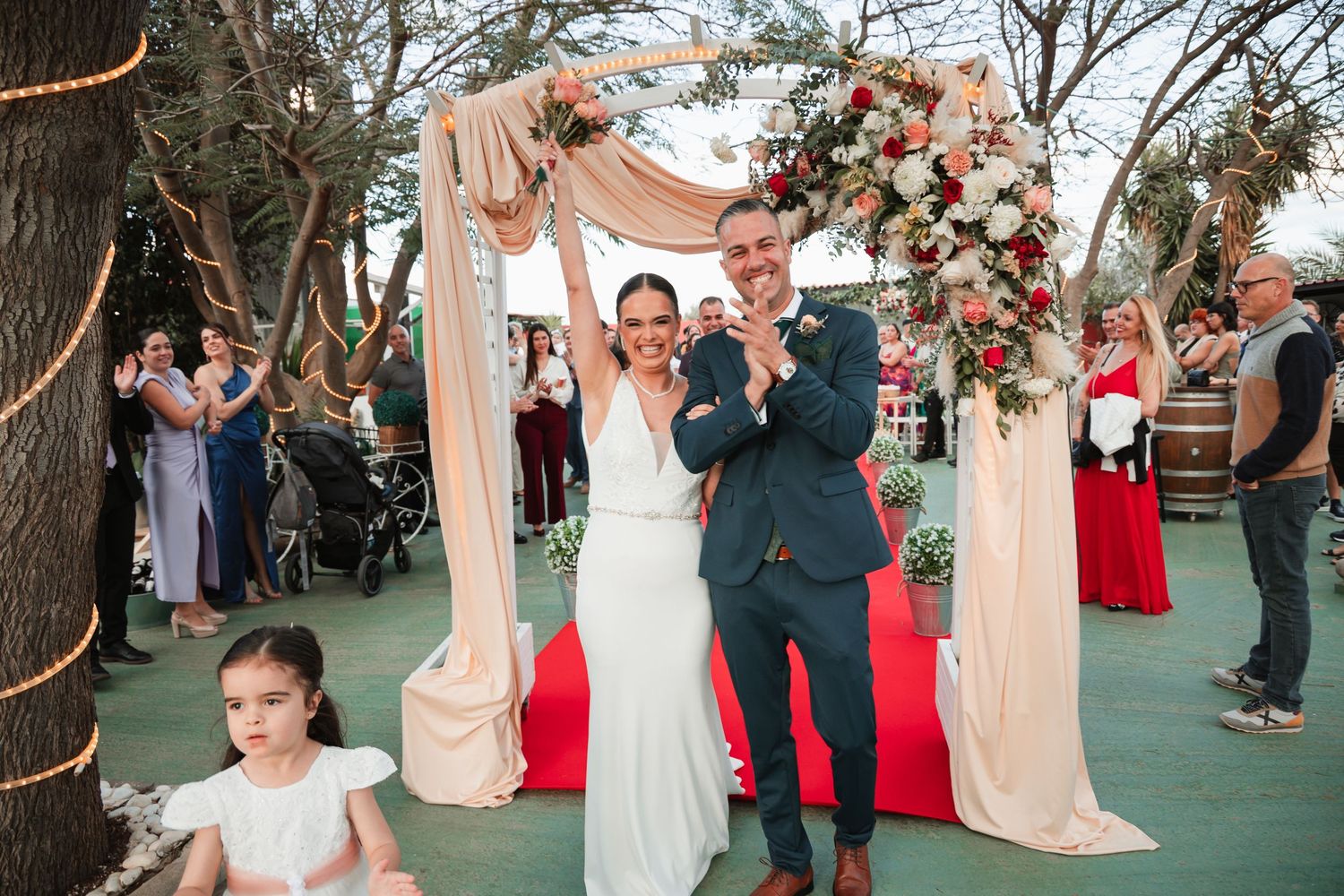 Wedding guests watching ceremony on a green lawn with decorative lighting.