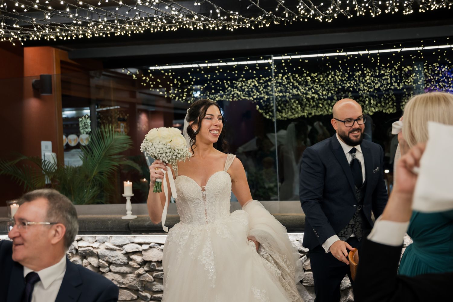 Wedding celebration with guests dancing under twinkling lights at an indoor reception.