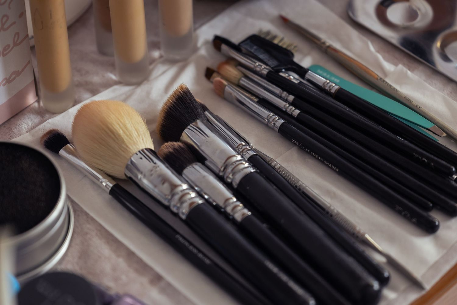 Professional makeup brushes and tools arranged on a light surface with a cream colored brush and black applicators.