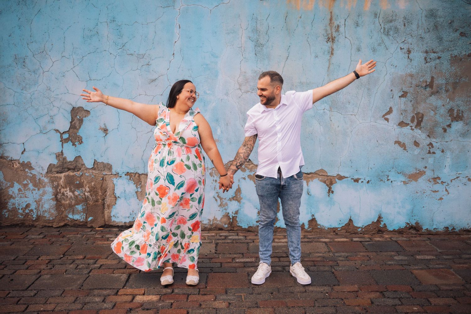 Playful couple posing against a weathered blue wall background.