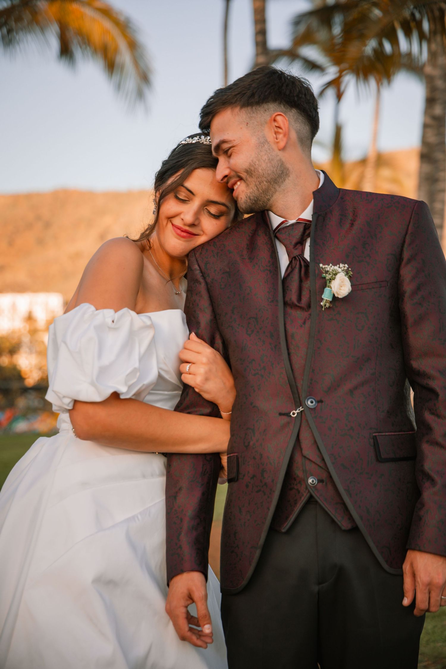 A couple shares a tender moment at sunset with palm trees in the background.