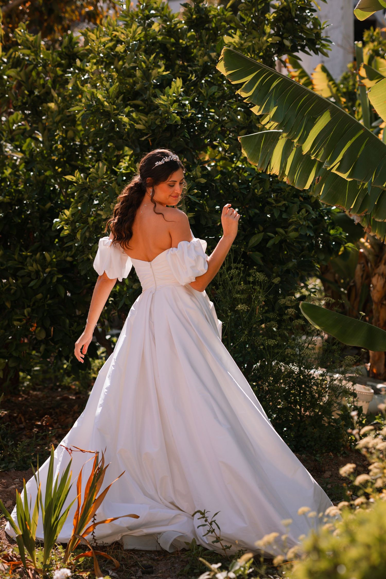 Flowing white wedding dress twirls in lush garden setting with tropical foliage.