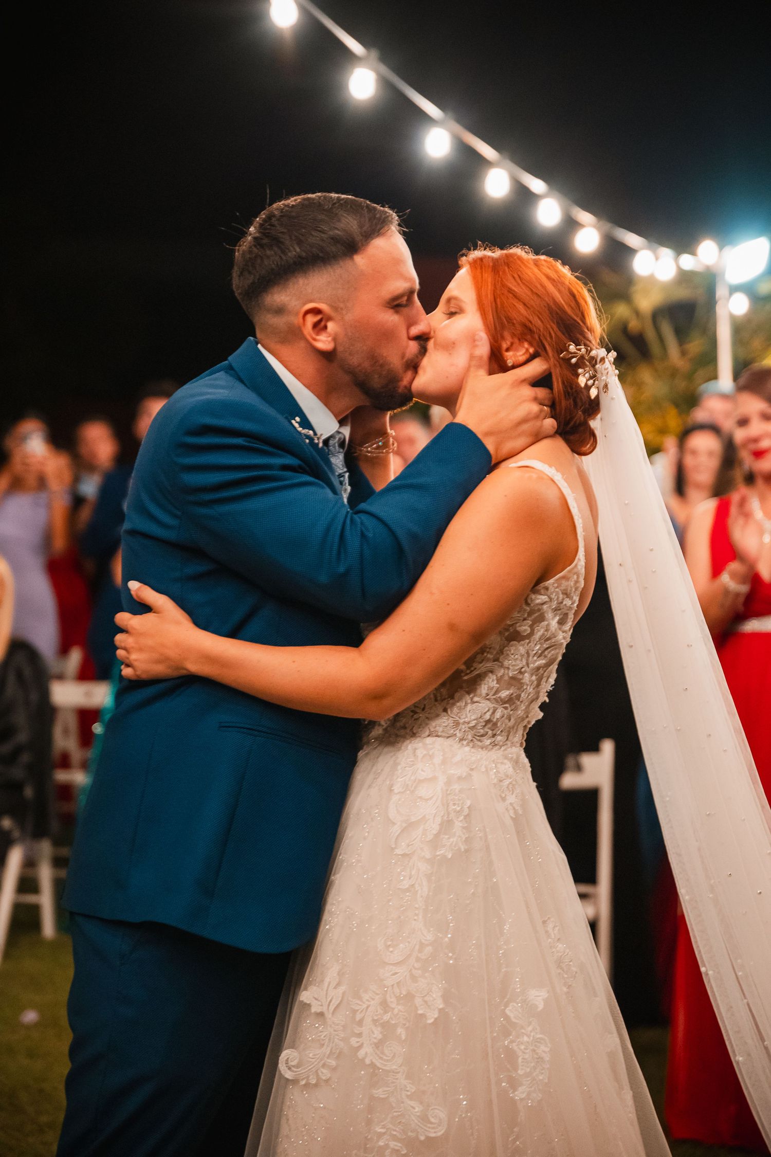 Romantic evening wedding kiss under twinkling string lights.