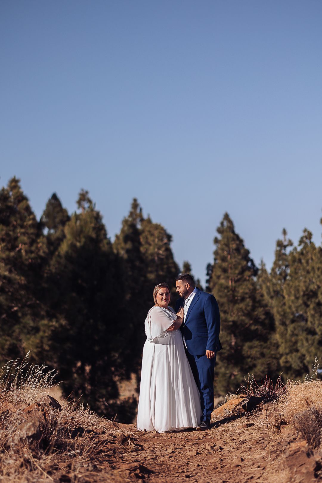 Wedding couple walking together on a desert trail surrounded by pine trees.
