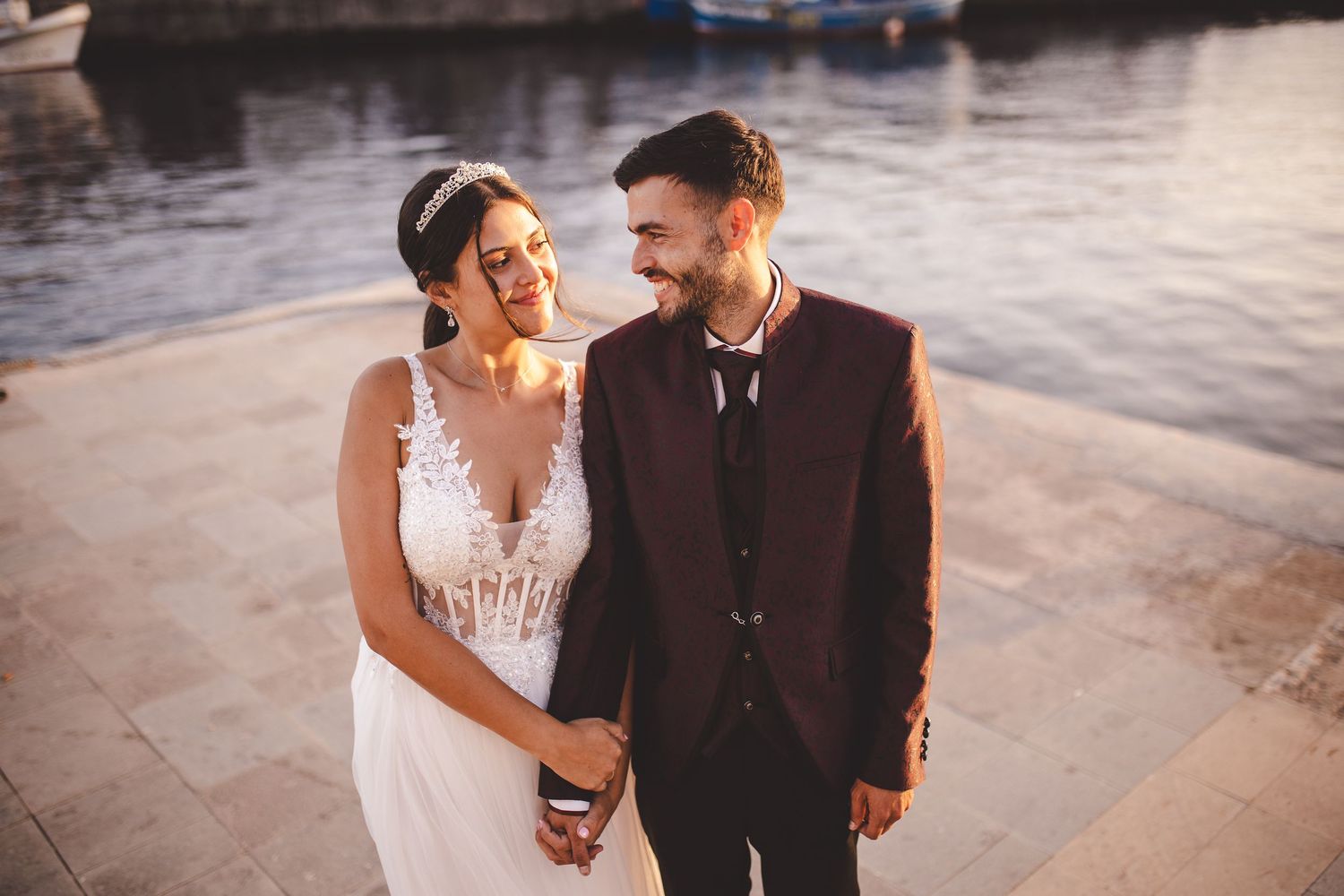 A romantic sunset portrait of newlyweds laughing together by the water.
