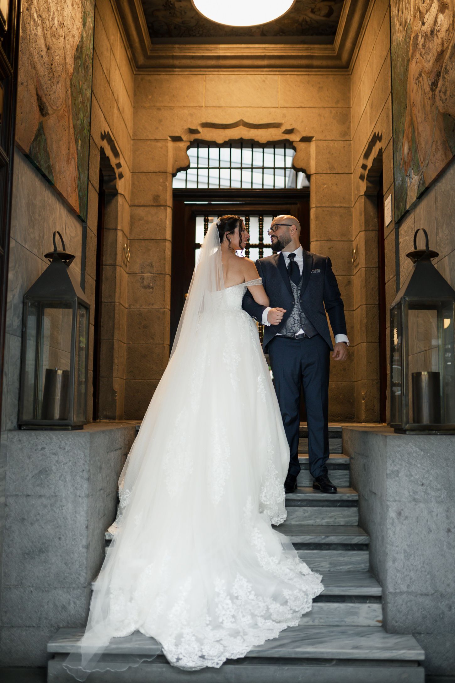 A flowing white wedding dress train trails elegantly across a stone hallway floor.