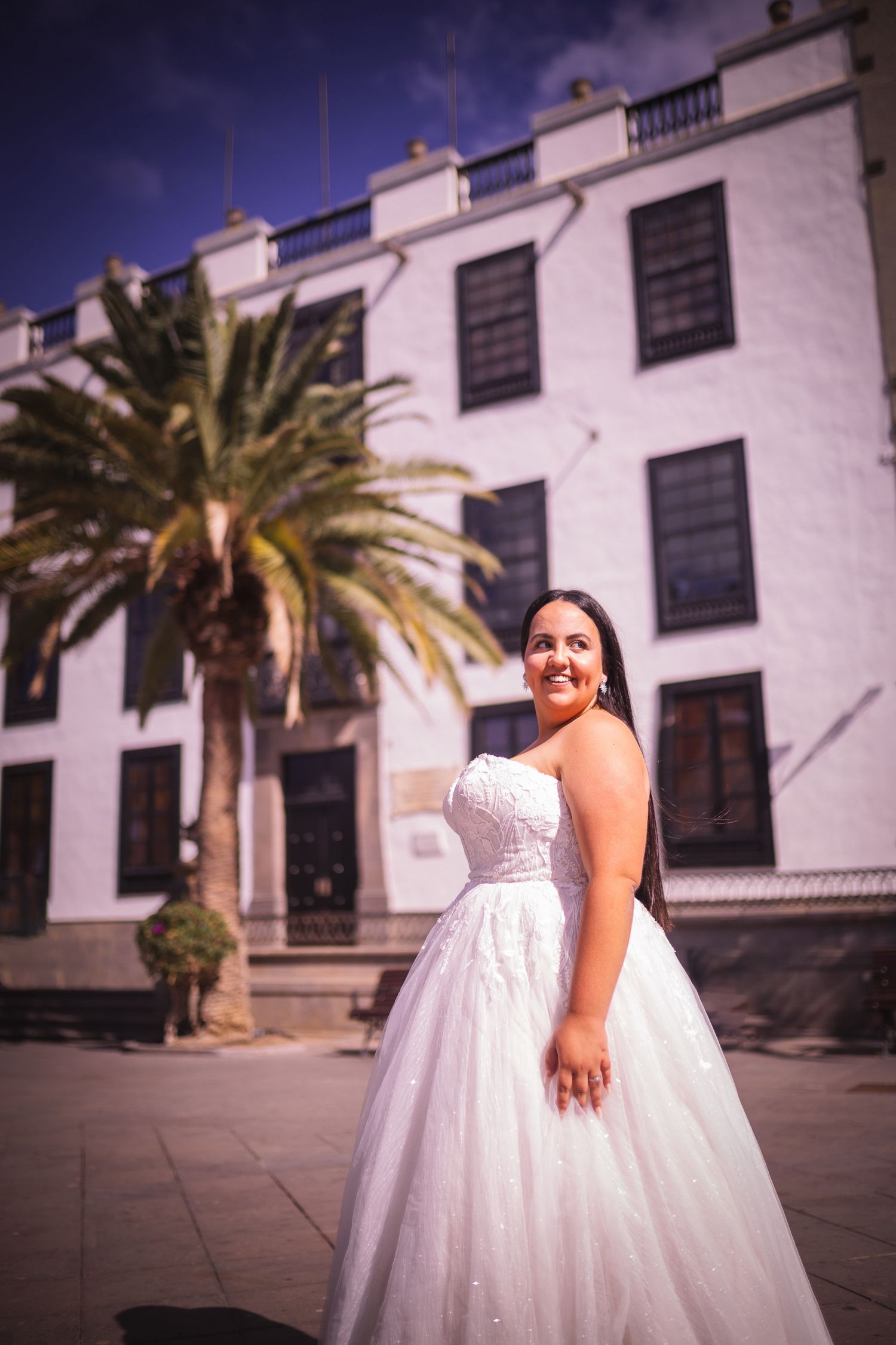 Elegant white wedding dress photographed against historic white colonial architecture with palm trees.