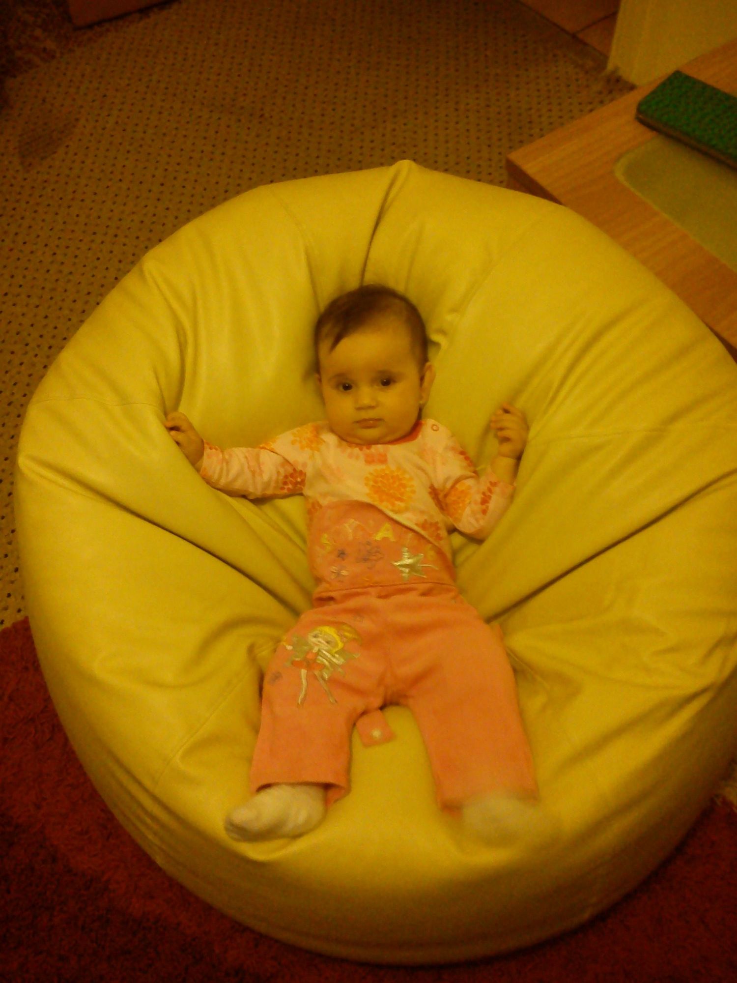 An infant wearing orange clothing relaxing on a large yellow bean bag chair.