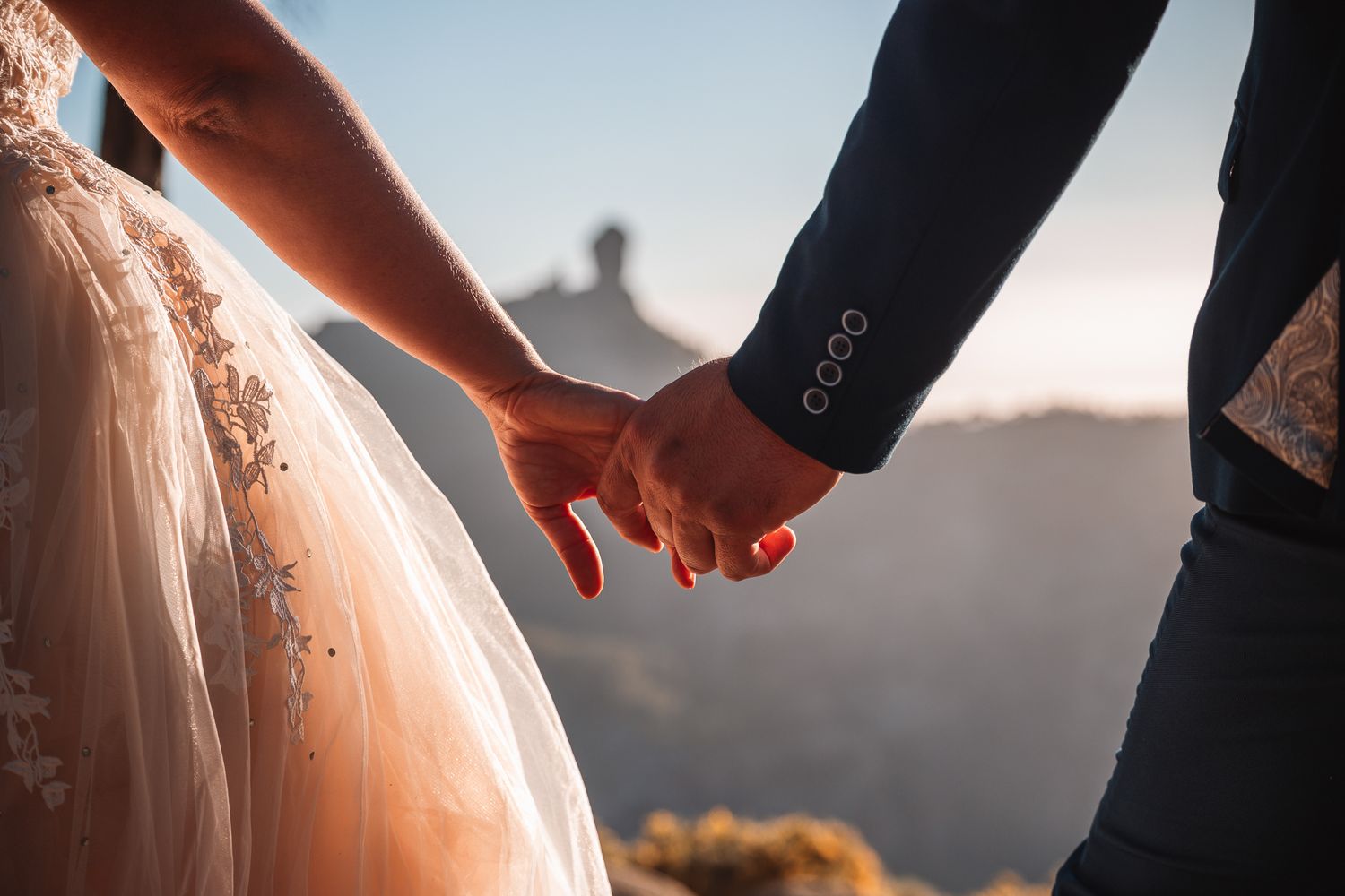 Close-up details of a lace wedding dress with delicate embroidery patterns against a sunset backdrop.