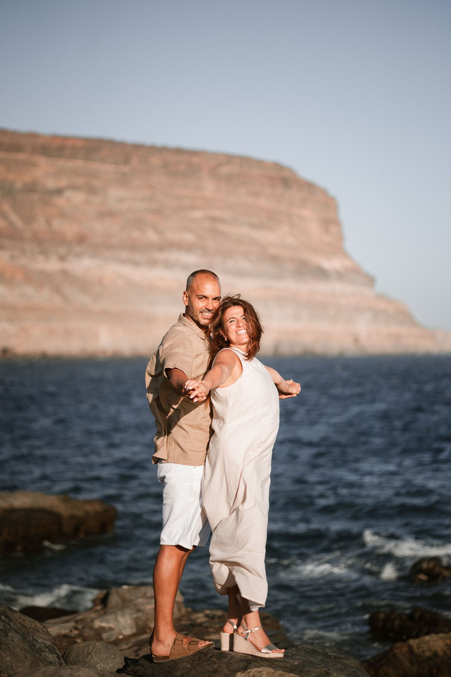 Romantic seaside photoshoot with coastal cliffs and ocean waves in the background.