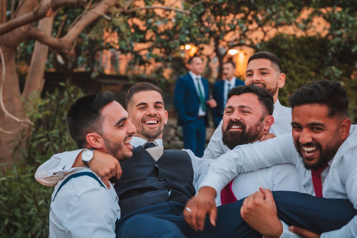 Groomsmen share laughs and hugs during outdoor wedding celebration.