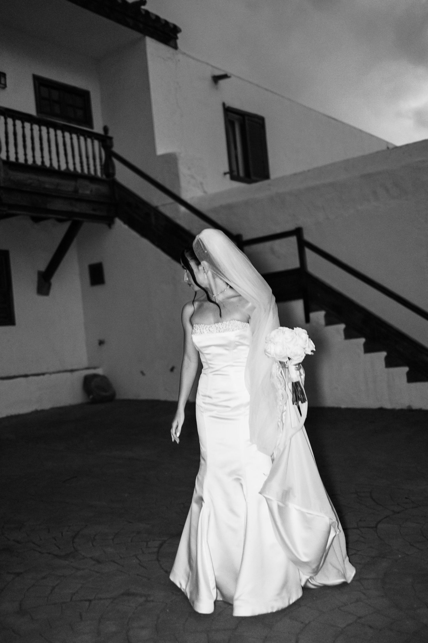 A black and white photo captures movement of a flowing white wedding dress on a textured floor.