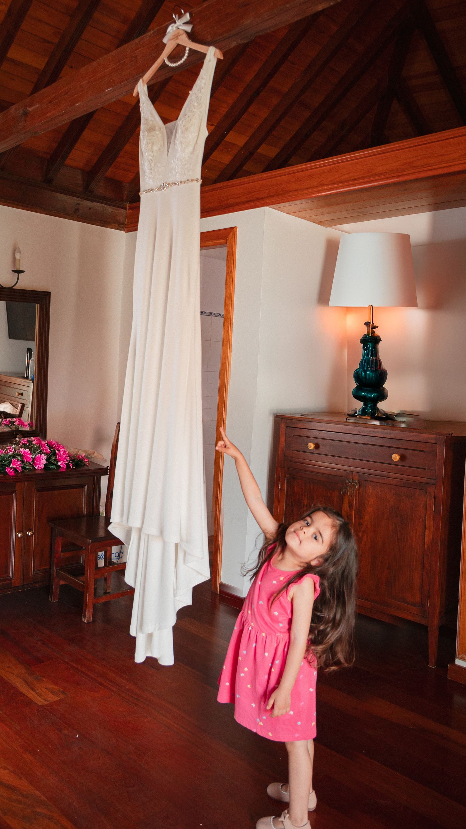 White wedding dress hangs elegantly in a rustic room with wooden beams and hardwood floors.