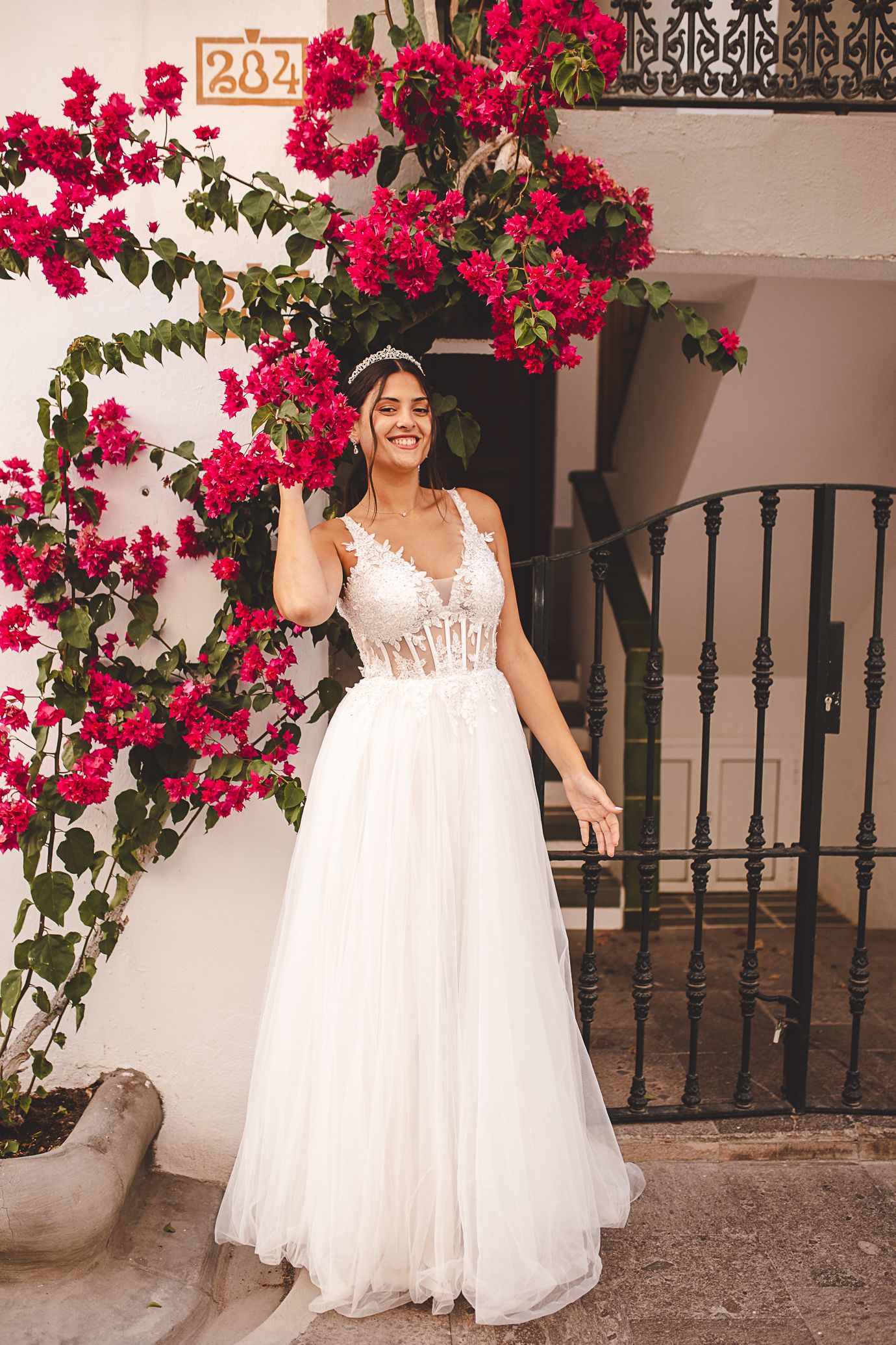 Bride in flowing white gown poses by vibrant pink bougainvillea flowers.
