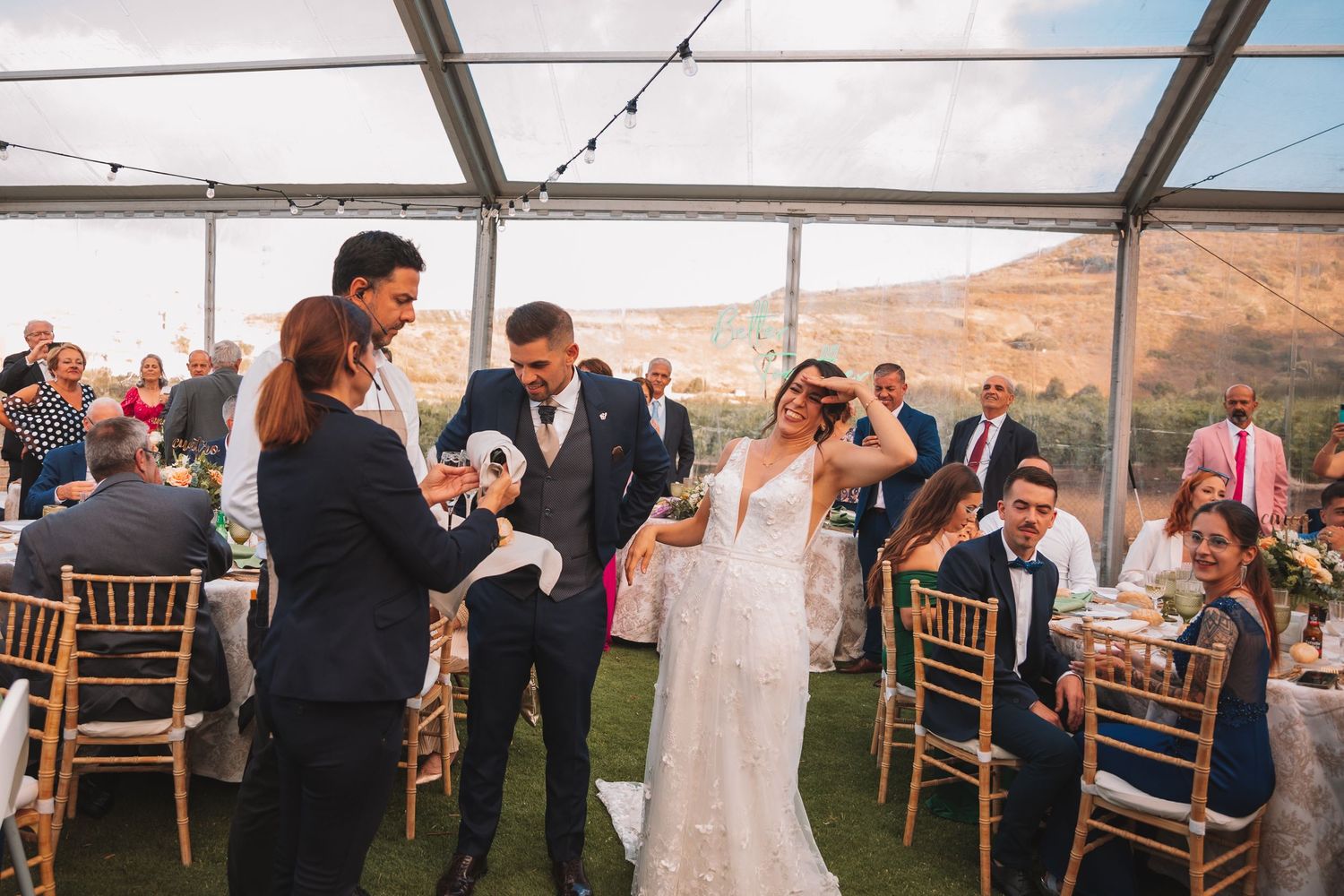 Wedding reception under a white tent with wooden chairs and mountain views.