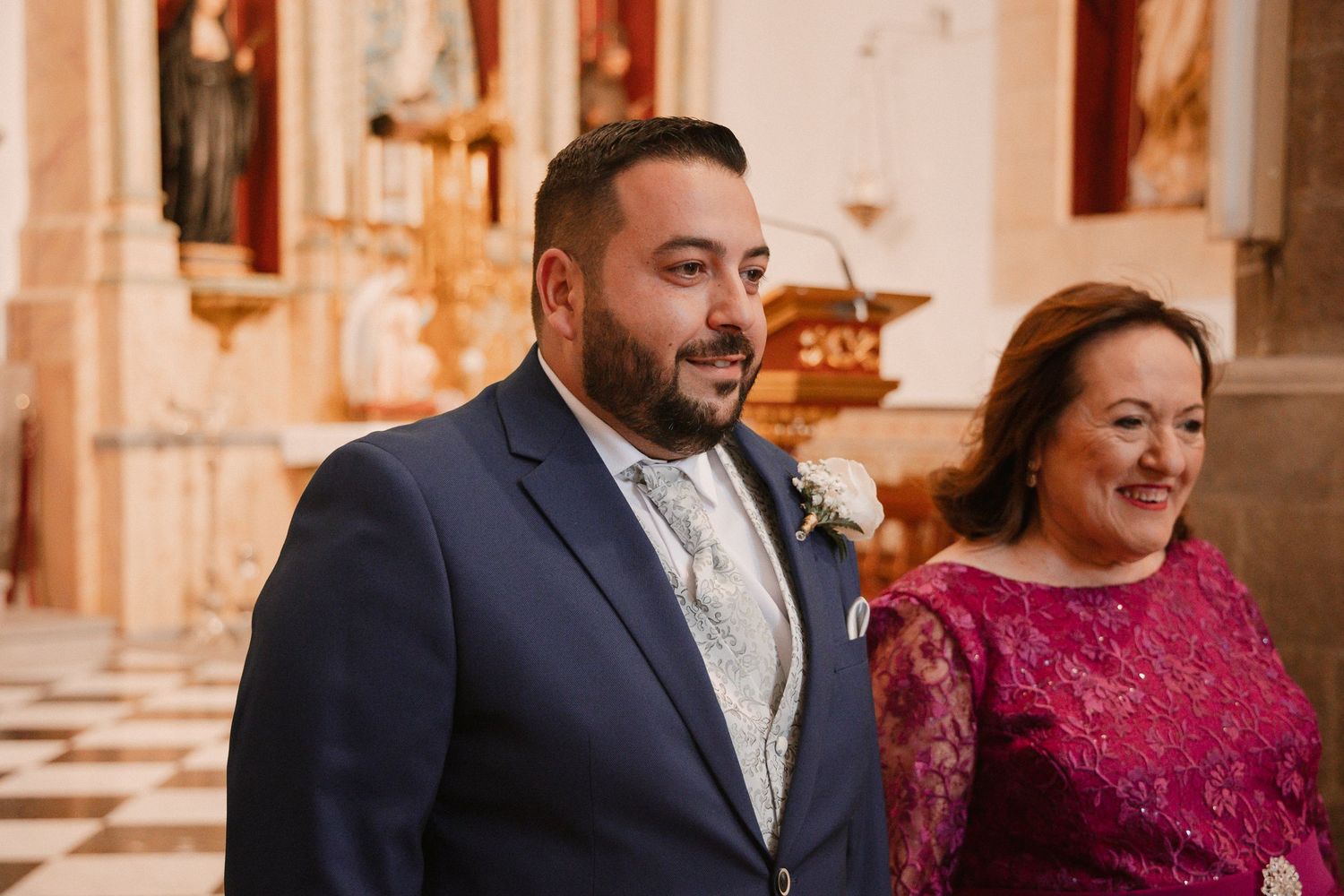 Wedding ceremony attendees seated in ornate church pews with decorative wood details.
