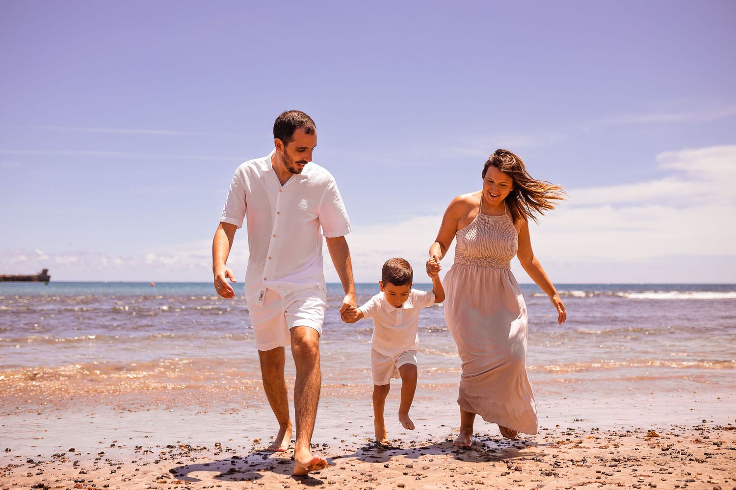 Family playing together on a sandy beach with blue ocean waves.