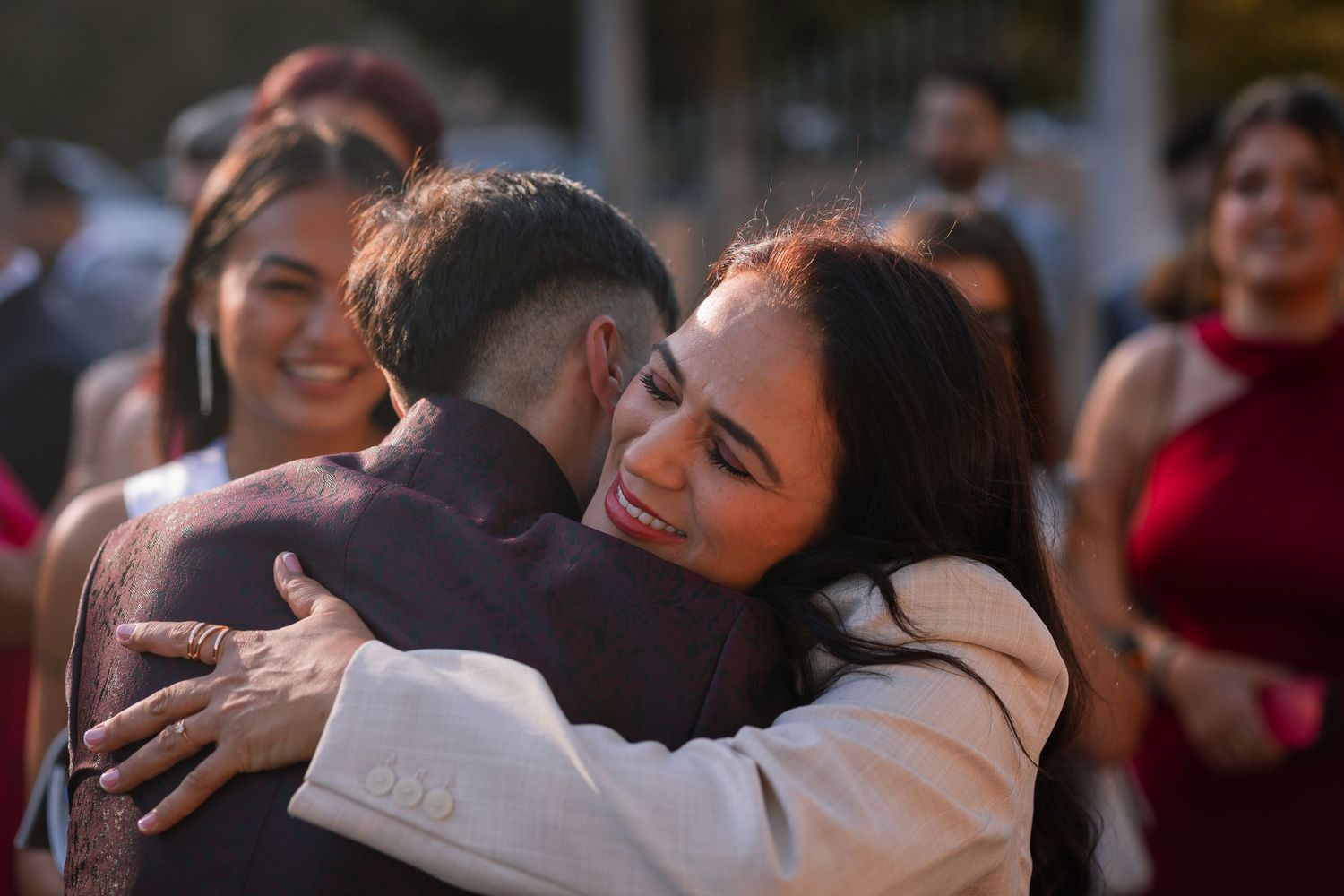 A warm embrace shared between two people at an outdoor celebration with guests in the background.