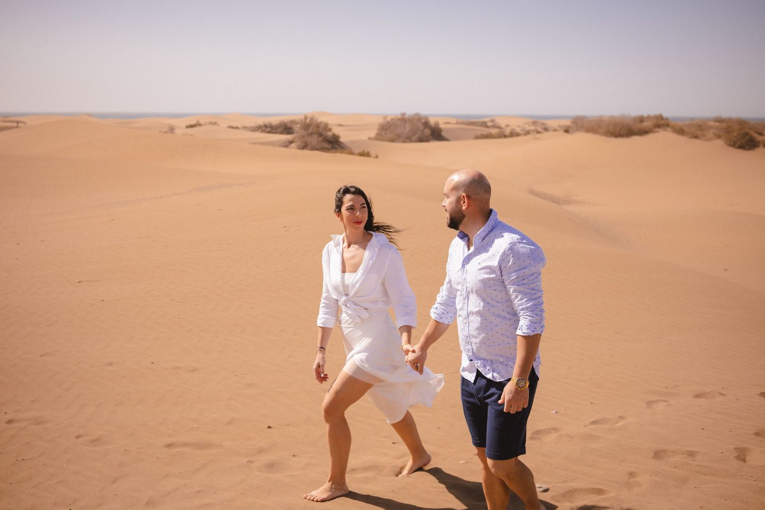 Two people running and playing in sand dunes during a desert photoshoot.