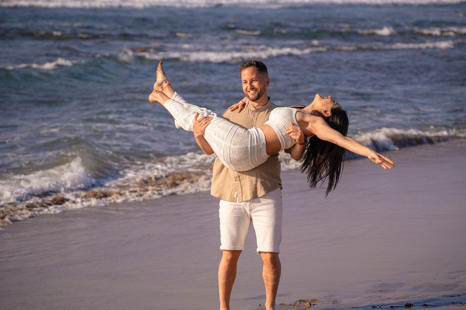 Playful beach moments captured as waves crash behind the couple.