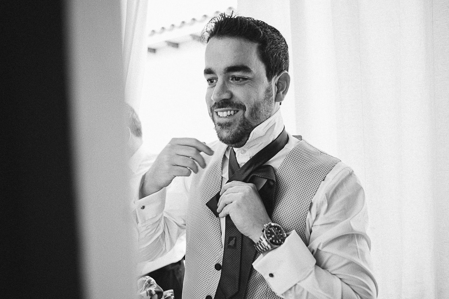 Black and white portrait of groom adjusting his tie before the ceremony.
