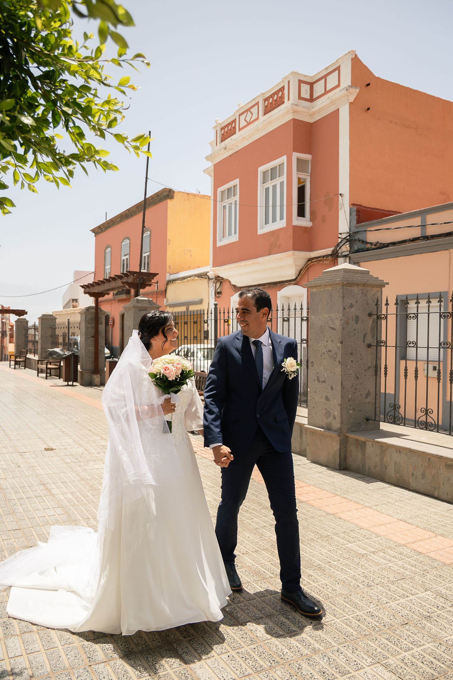 A couple shares a romantic moment on a sunlit terrace with terracotta buildings.