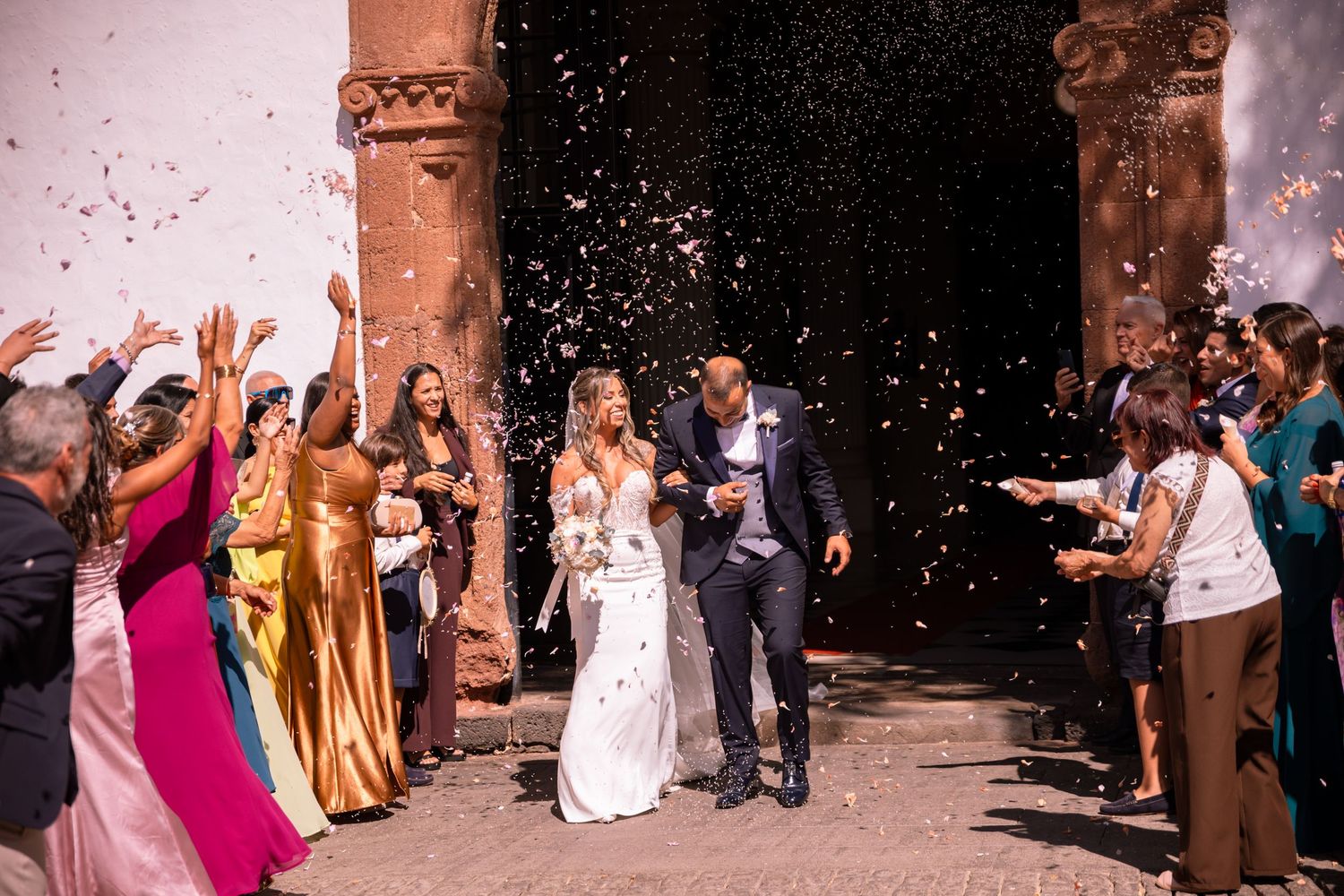 Wedding guests throwing confetti at a celebration outside a building with stone columns.