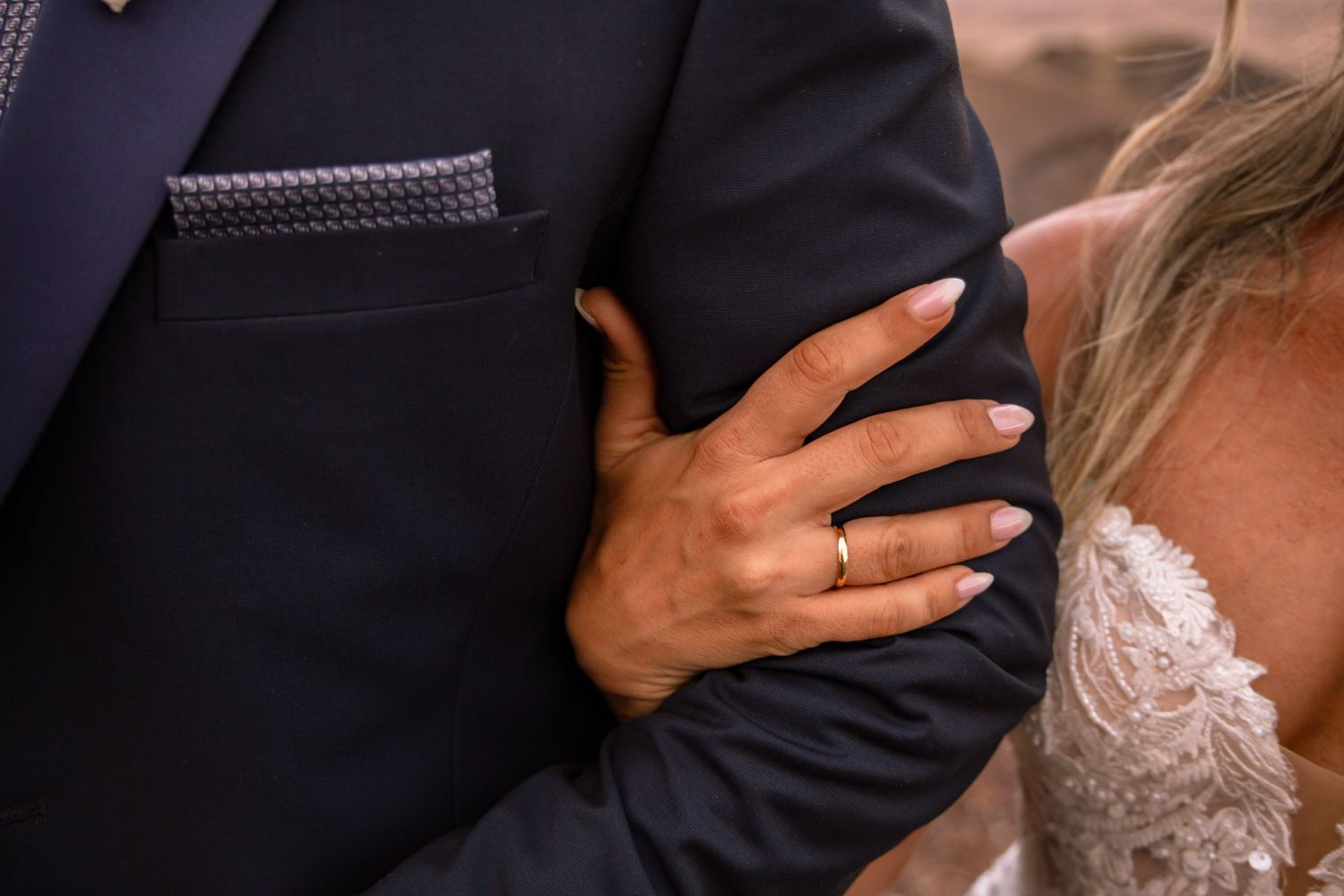 Close-up details of formal attire and hands during what appears to be a wedding ceremony.