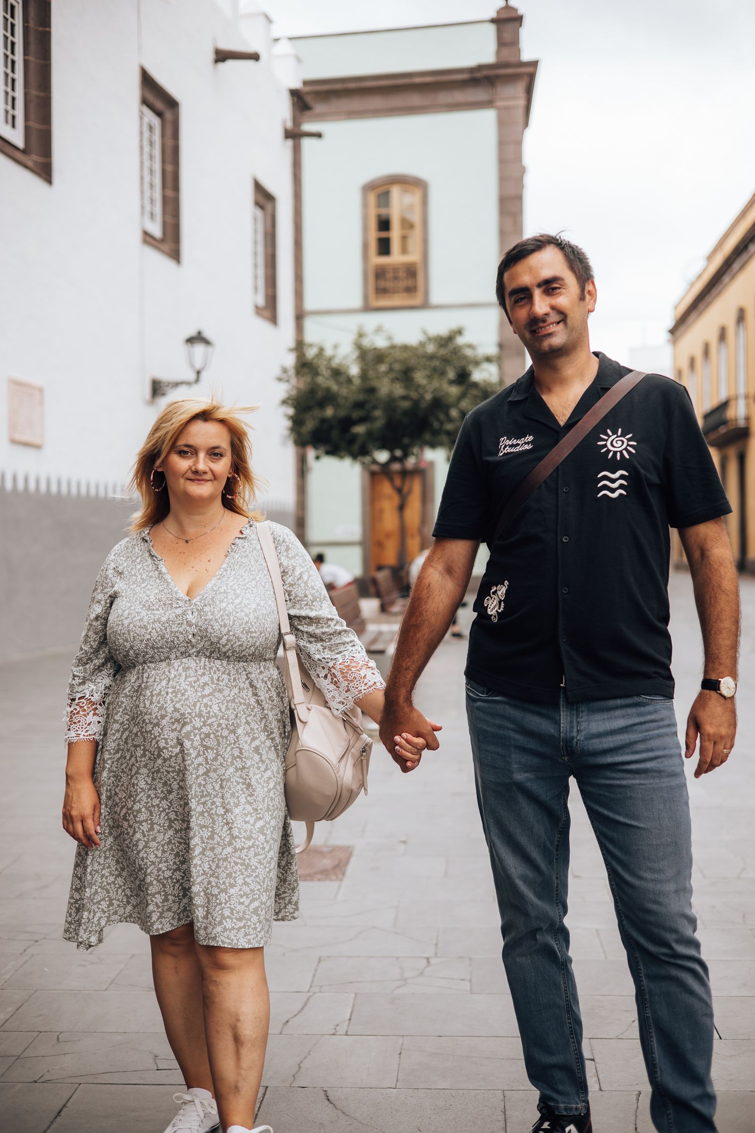 A couple walking together on a stone paved street, with the woman wearing a floral dress.