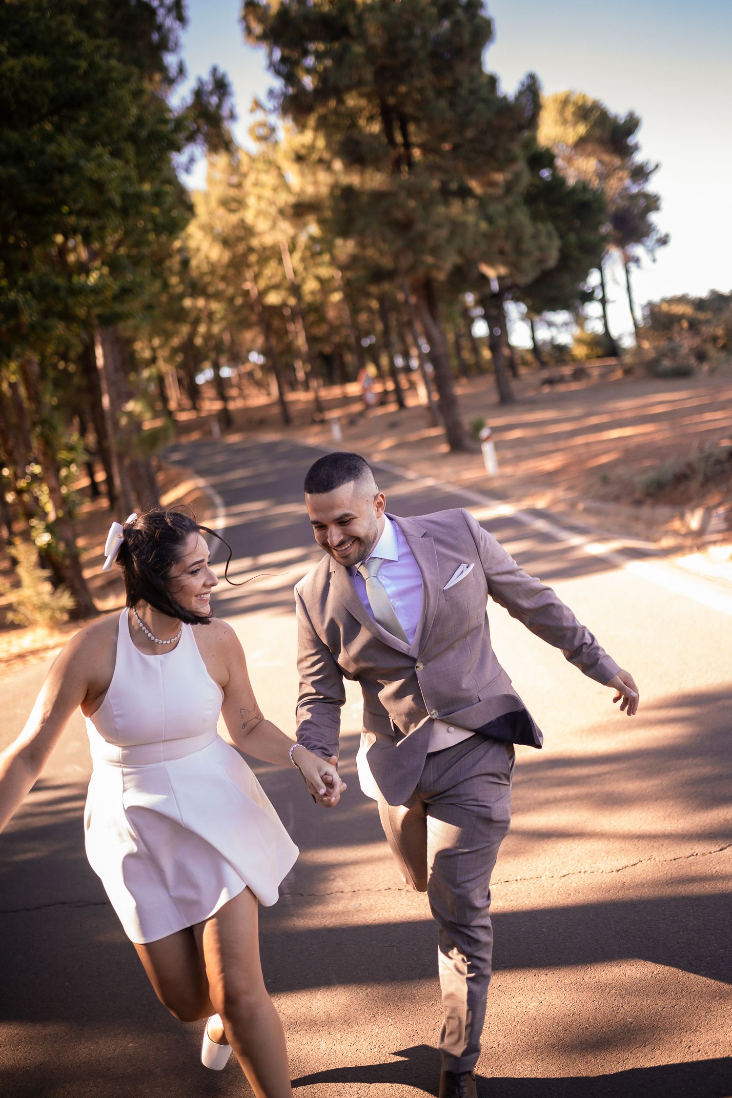 A playful couple dances together on a sunlit outdoor path.