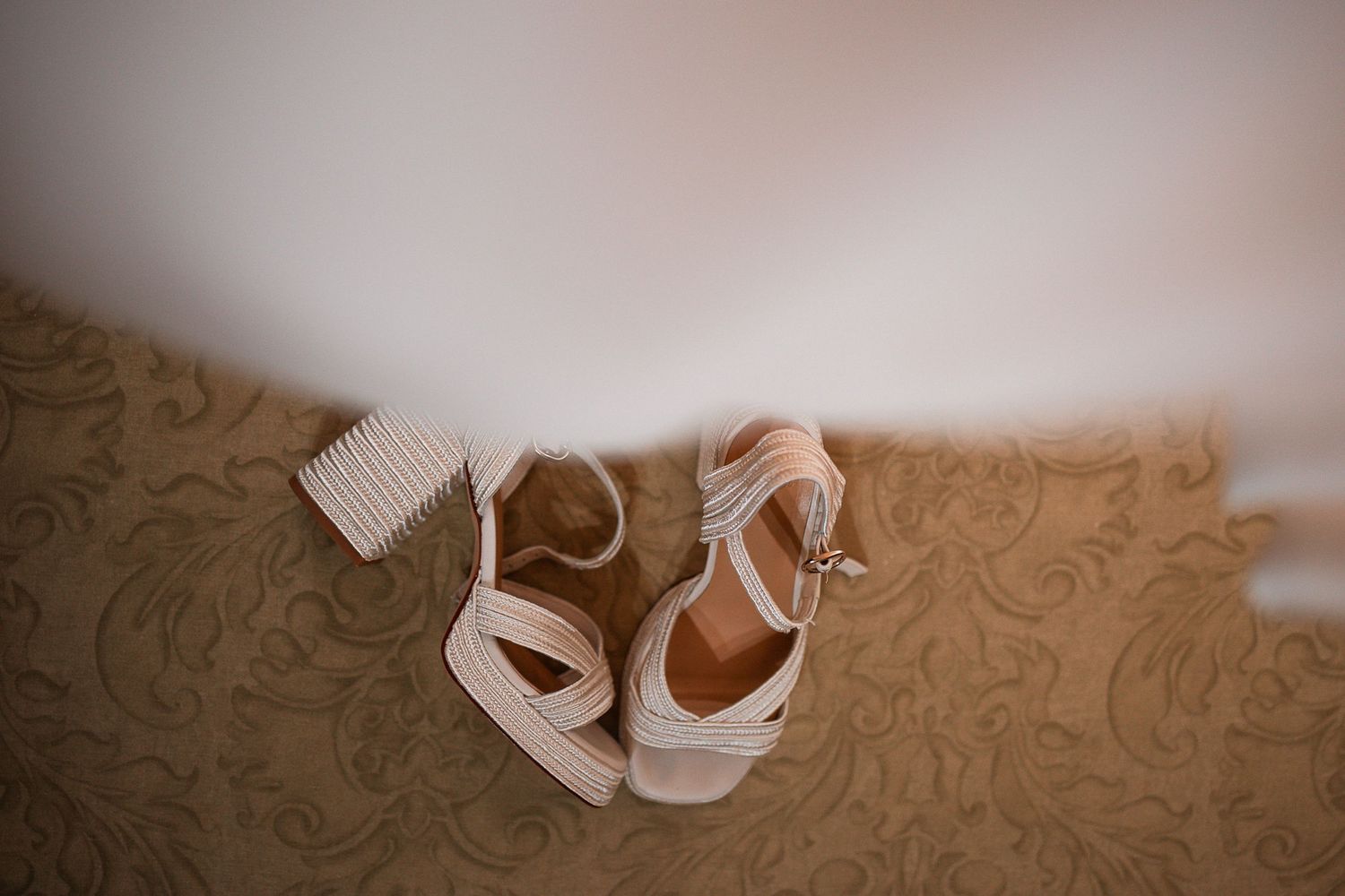 Delicate nude wedding shoes arranged on textured carpet.