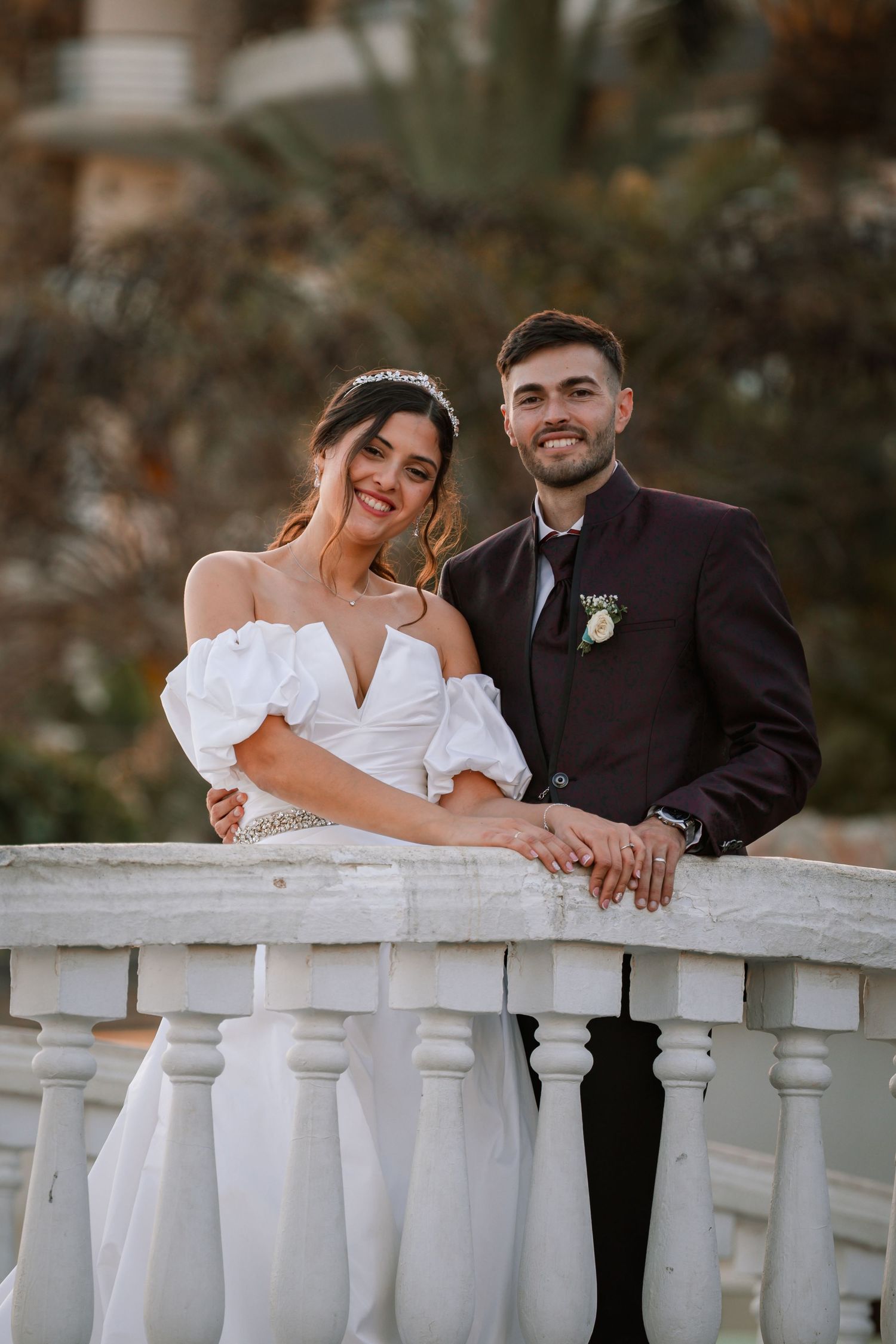 Romantic wedding couple leaning on white balustrade during outdoor photo session.