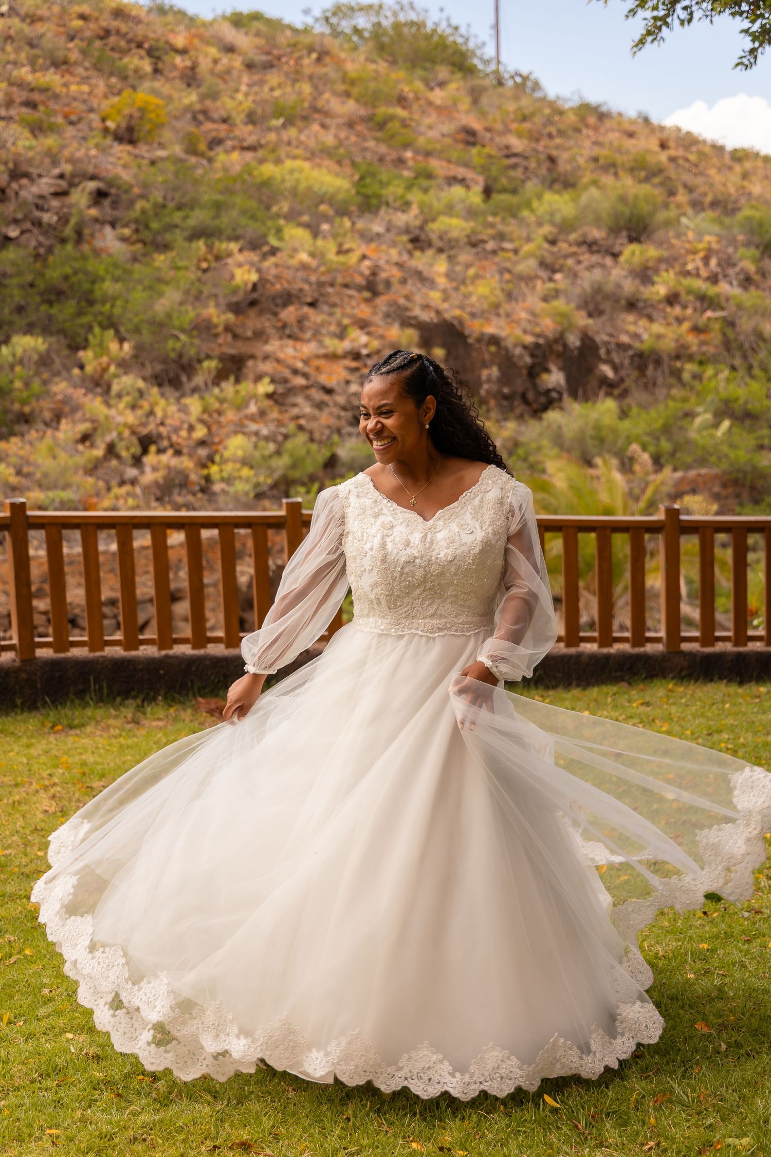 Bride in lace wedding gown twirls on grass with mountains in background.