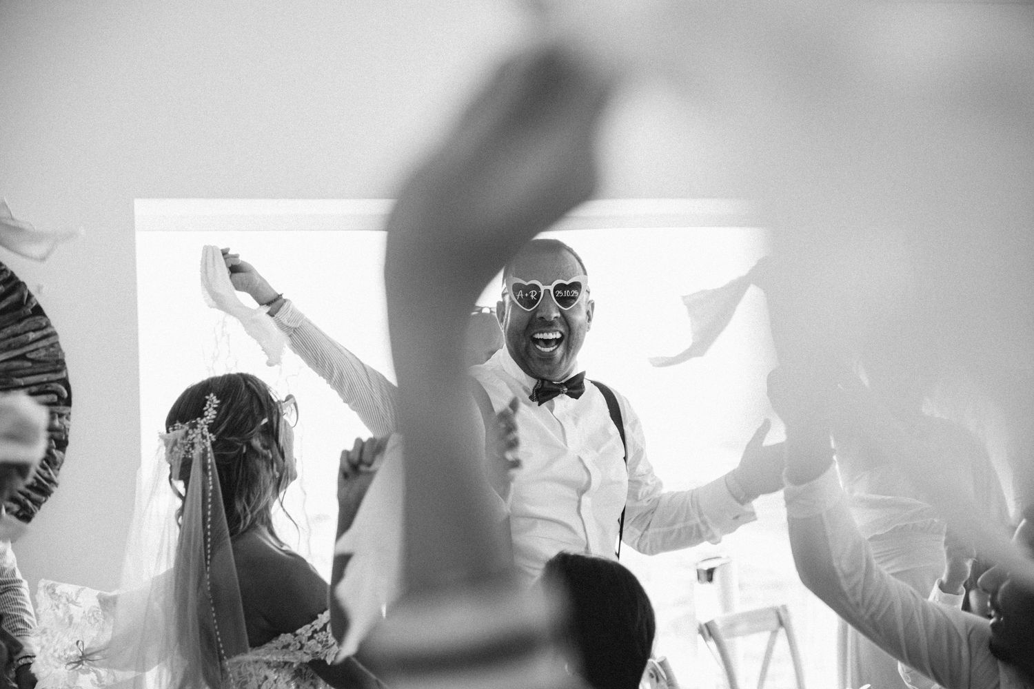 Black and white photo of wedding guests dancing and celebrating at a reception.