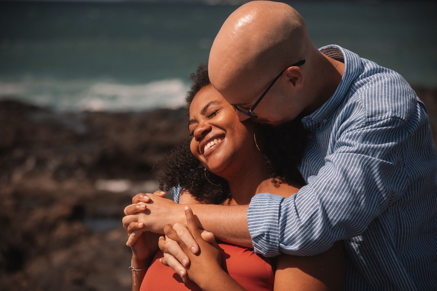 Intimate maternity photography session with couple embracing on a scenic beach.