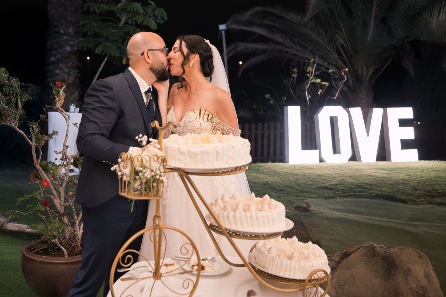 An elegant wedding cake display with illuminated LOVE sign in the background.