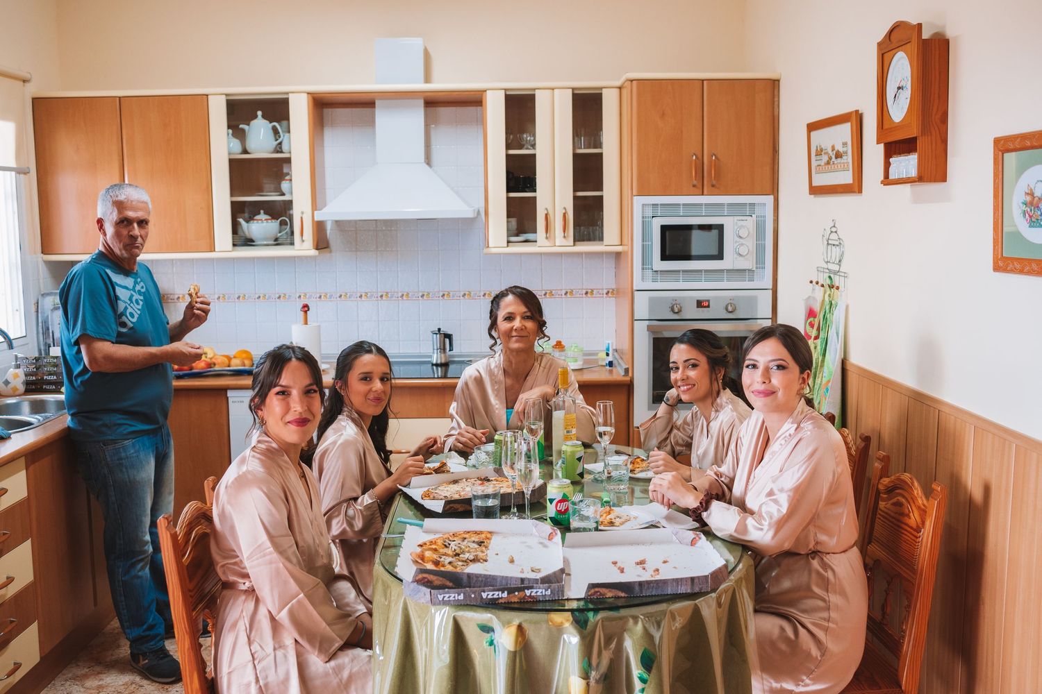 Family gathering around dining table in warm-toned kitchen setting.